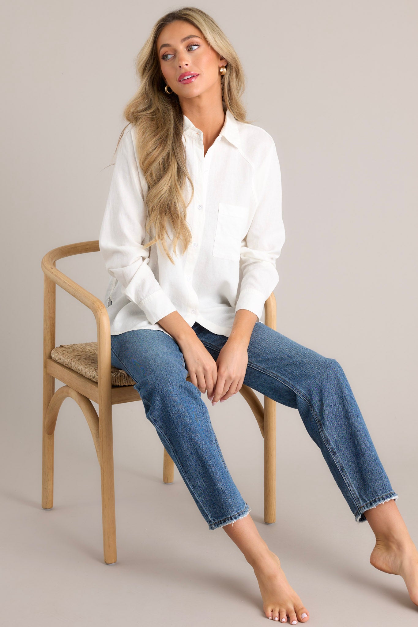 Seated front view of this white top that features a collared neckline, a functional button front, a breast pocket, button cuffed long sleeves, and a split high low hemline.