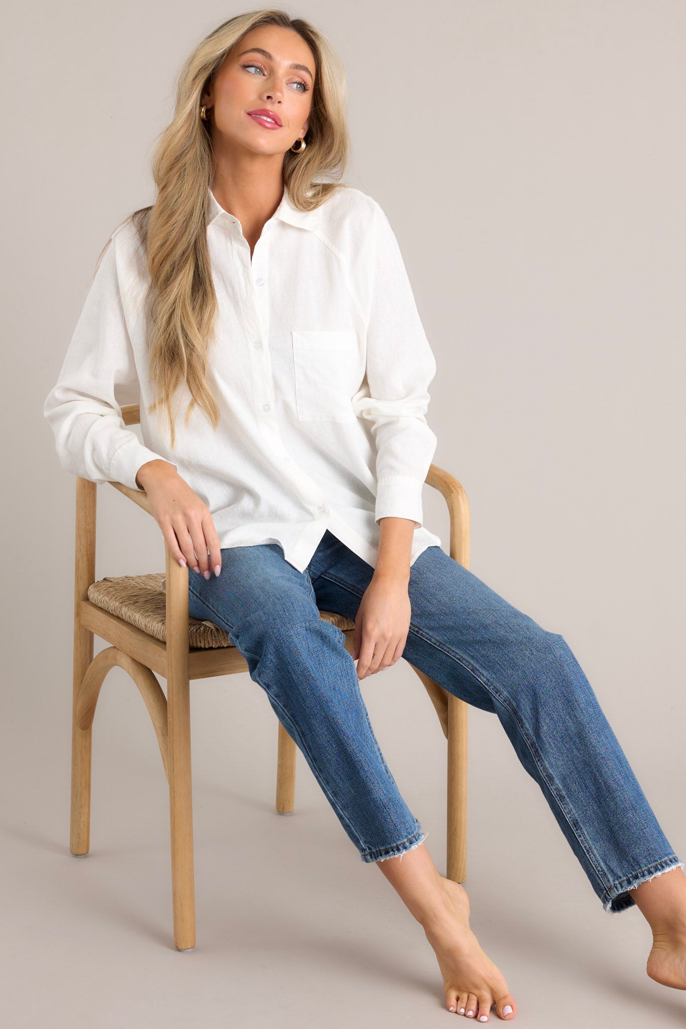 This white top features a collared neckline, a functional button front, a breast pocket, button cuffed long sleeves, and a split high low hemline.