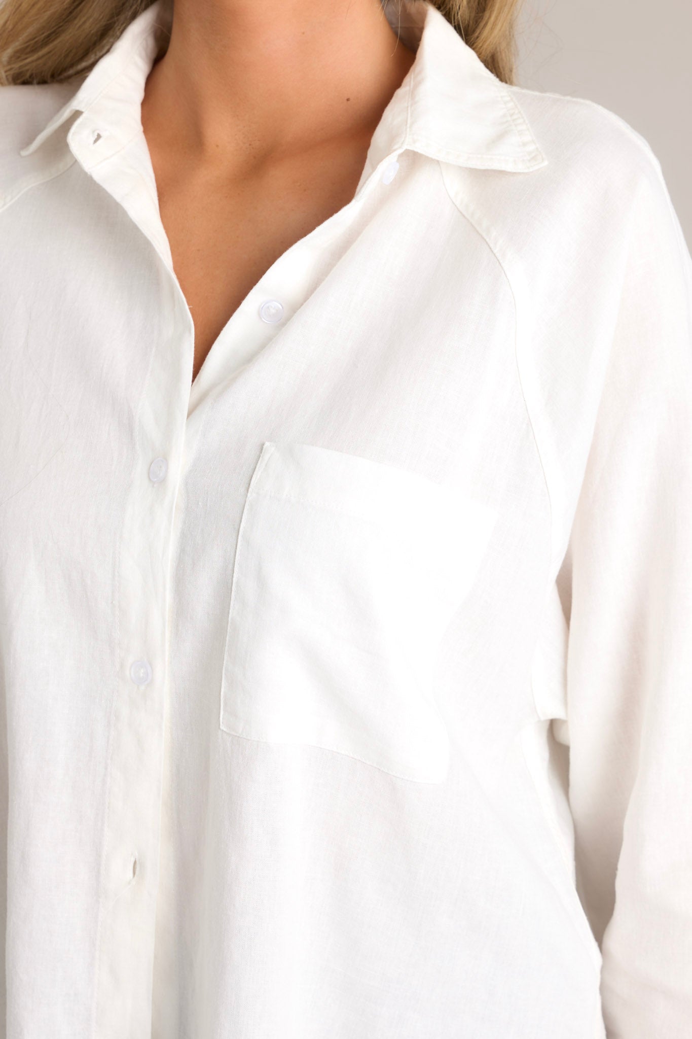 Close up view of this white top featuring a collared neckline, a functional button front, a breast pocket, button cuffed long sleeves, and a split high low hemline.