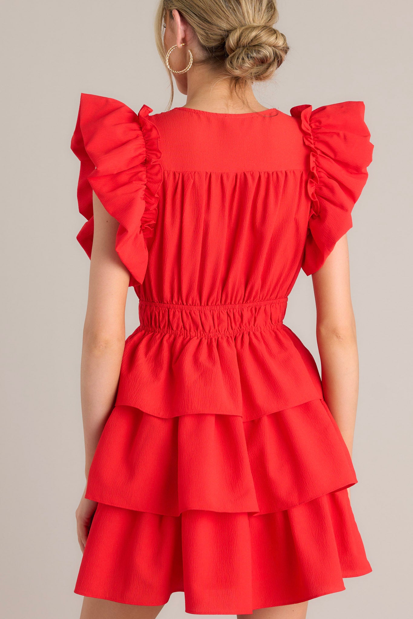 Back view of this Short red dress with a wrap-style V-neck, ruffled sleeve details, and a layered skirt