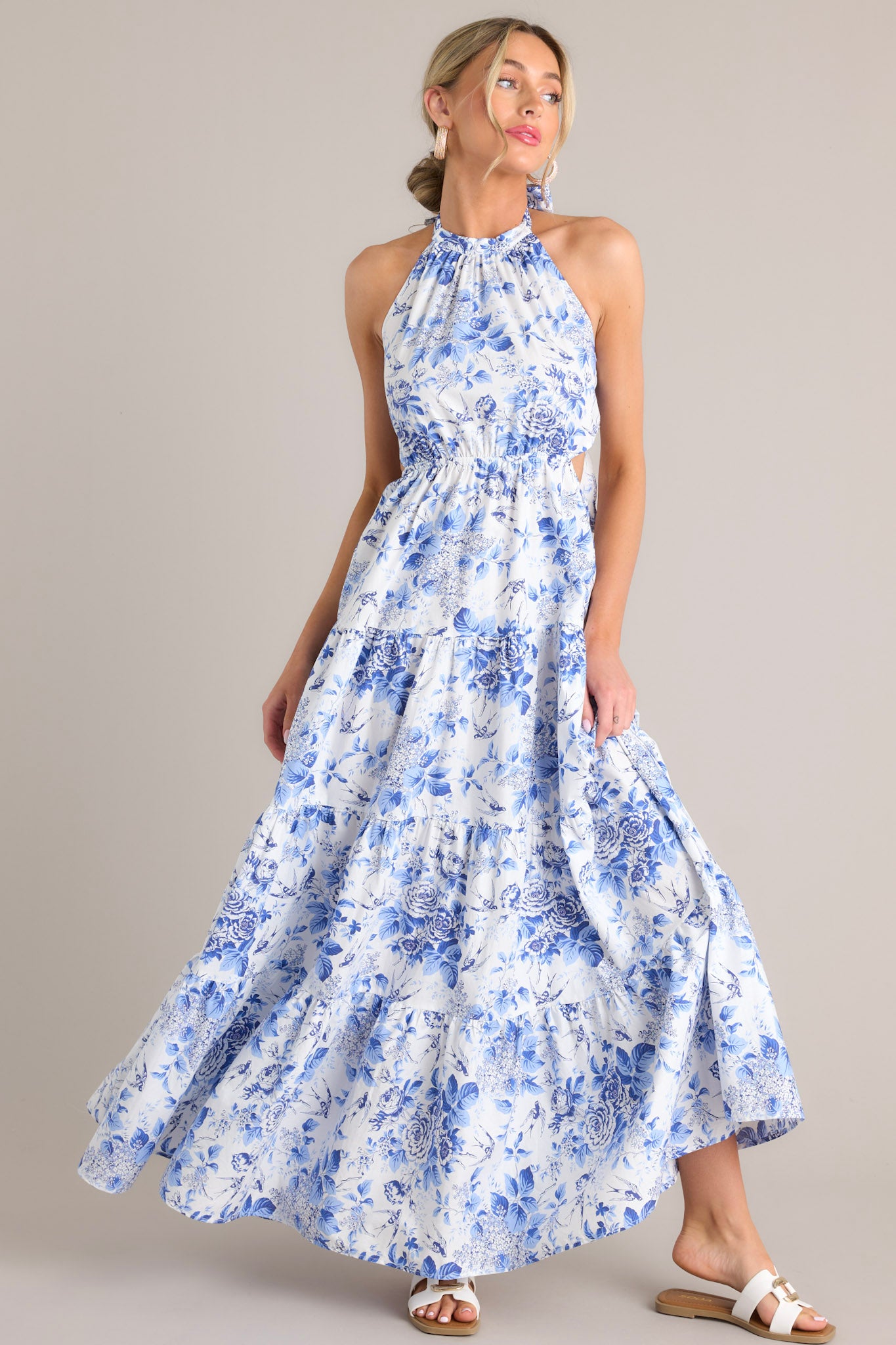 This floral maxi dress features a self-tie halter neckline, an open back, a self-tie back feature, an elastic waistband, side cutouts, and a tiered design.