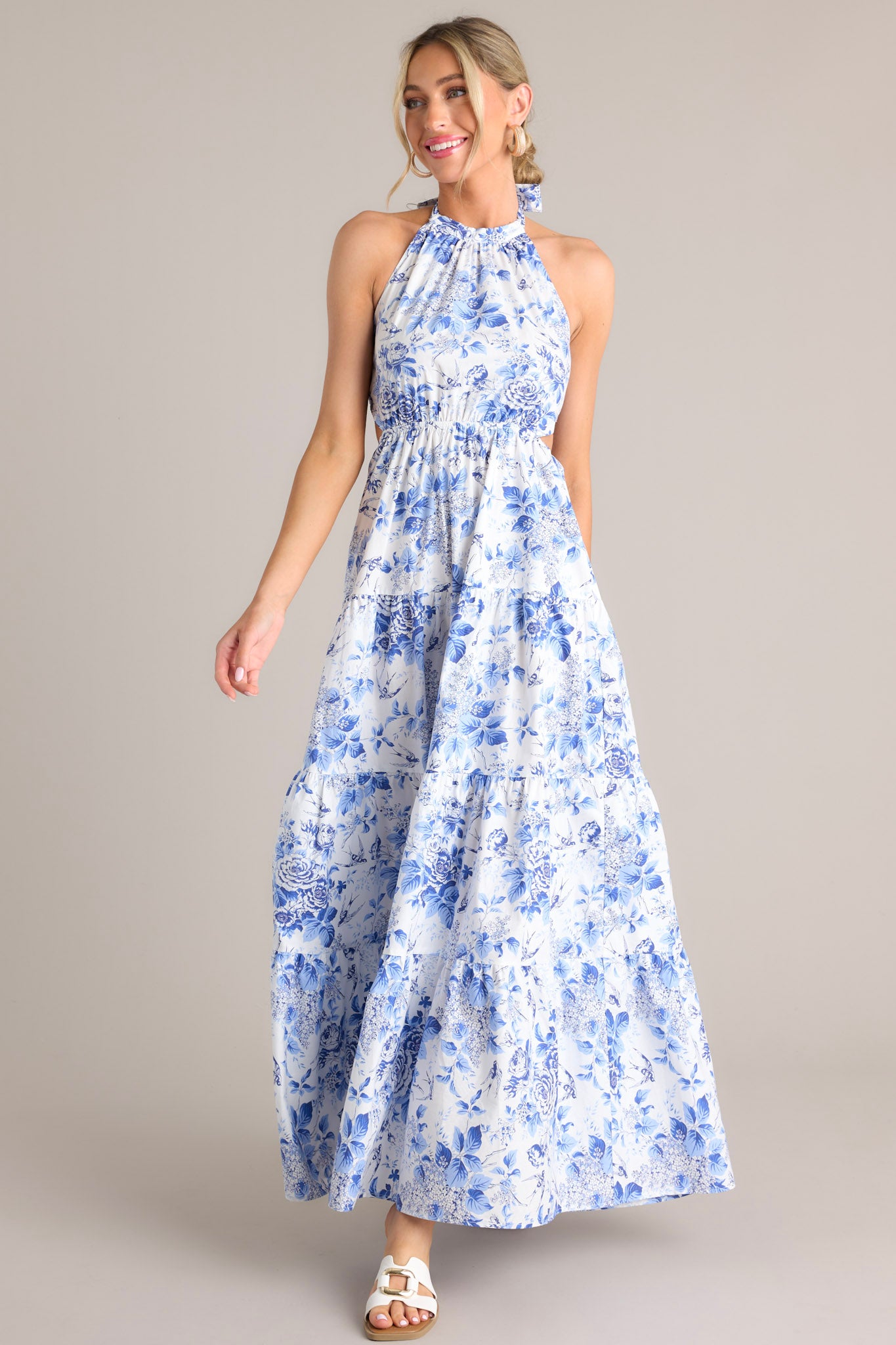 Full body view of this floral maxi dress that features a self-tie halter neckline, an open back, a self-tie back feature, an elastic waistband, side cutouts, and a tiered design.