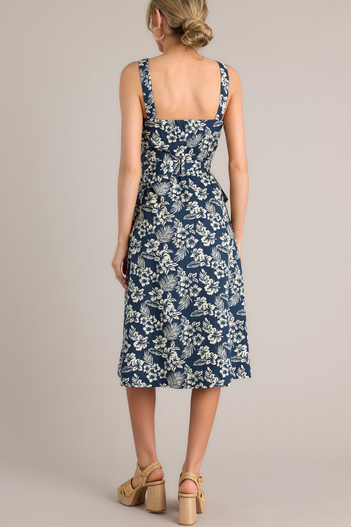 Back view of a navy midi dress showcasing the thick straps, self-tie waist belt with belt loops, and buttoned hip pockets.