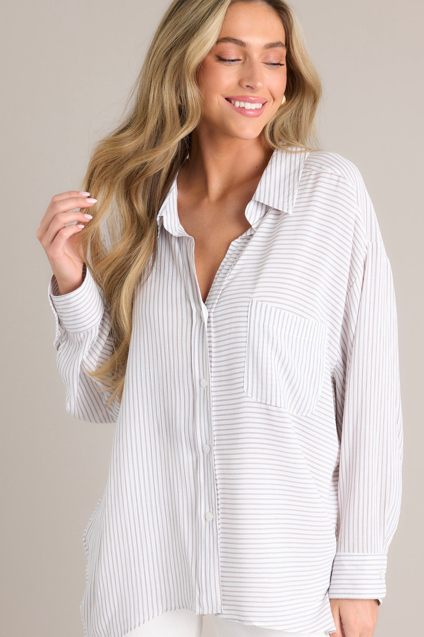 Close up front view of this white stripe top that features a collared neckline, a functional button front, a breast pocket, a unique stripe pattern going both vertically & horizontally, button cuffed long sleeves, and a split hemline.