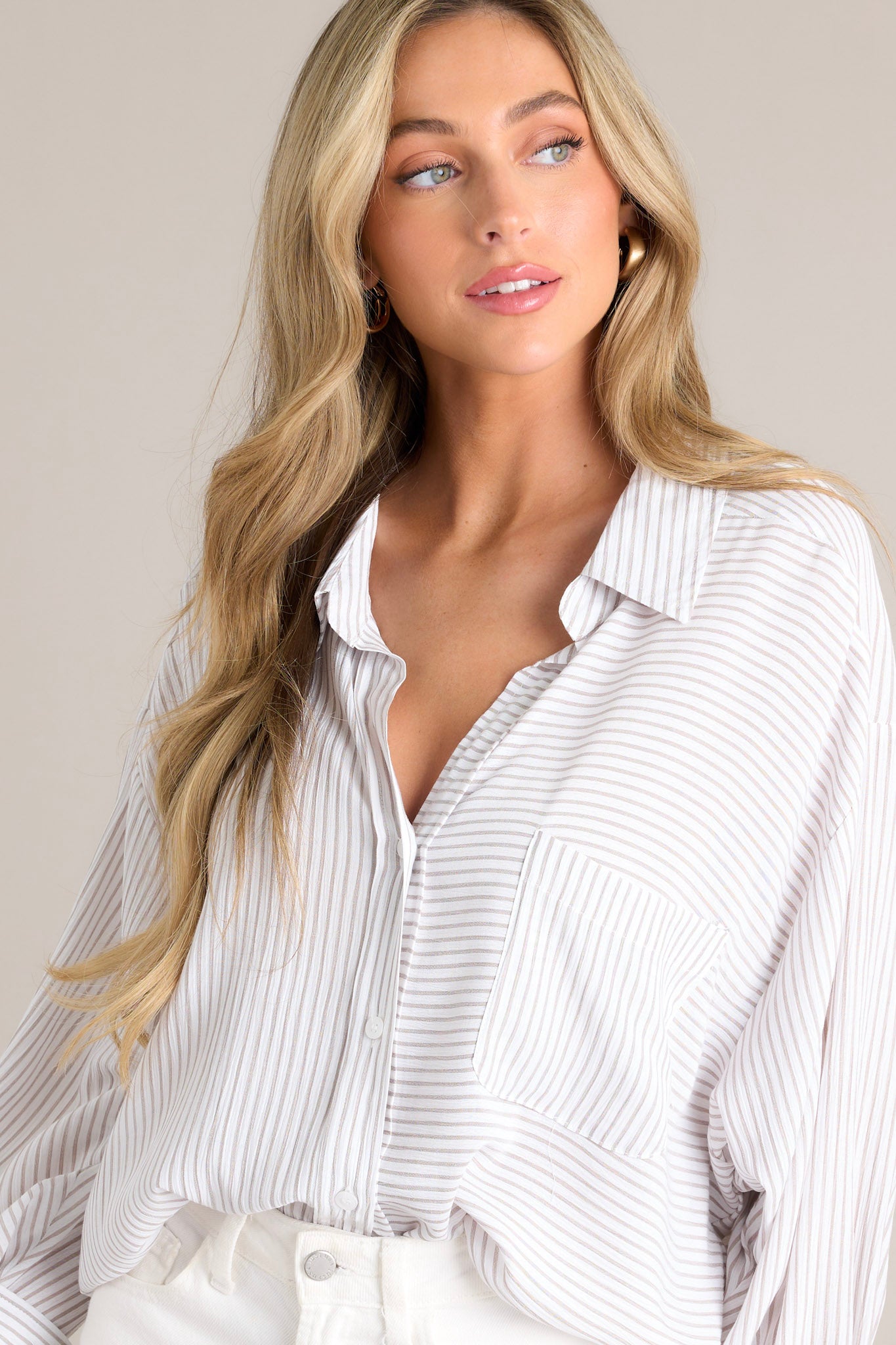 Angled front view of this white stripe top that features a collared neckline, a functional button front, a breast pocket, a unique stripe pattern going both vertically & horizontally, button cuffed long sleeves, and a split hemline.