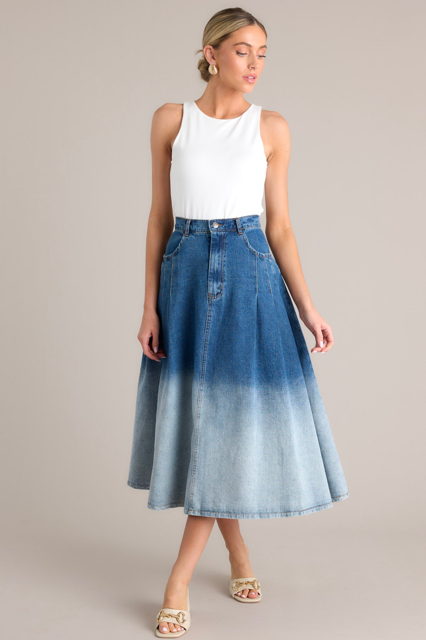 Angled view of this skirt that features a high waisted design, a classic button & zipper closure, belt loops, functional front pockets, subtle pleats, and an ombré gradient.