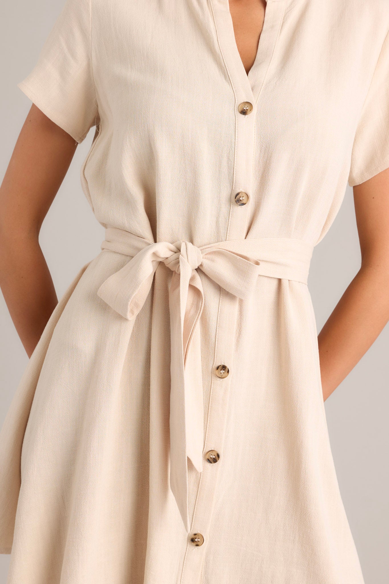 Close up view of this dress that features functional tortoise buttons down the front, an optional self-tie belt, short sleeves, and mini length.