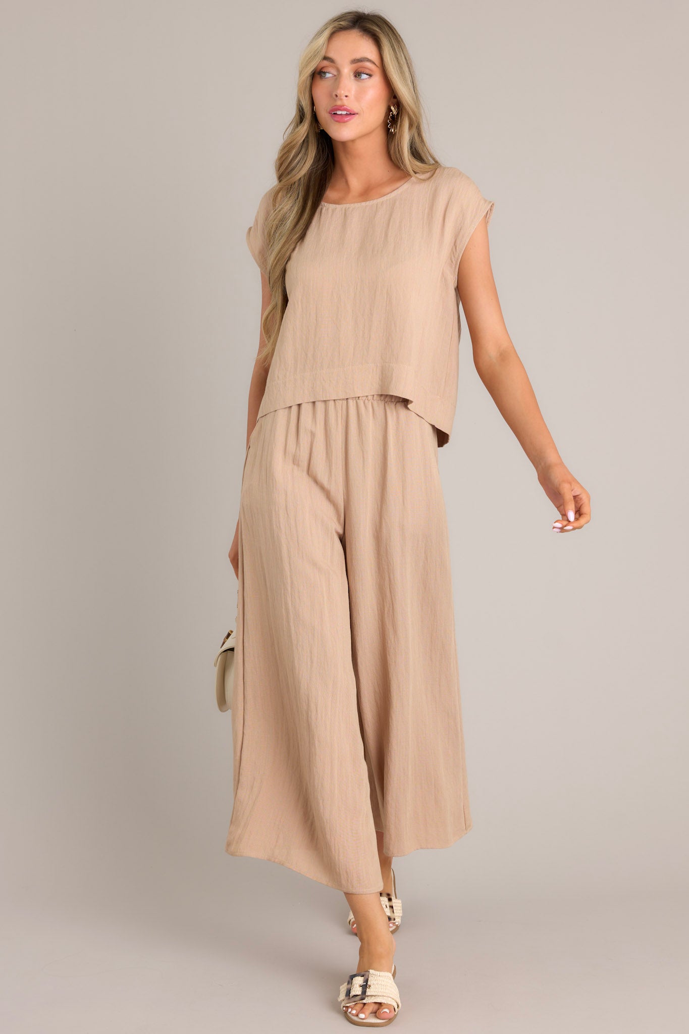 Full body view of this beige top featuring a cap sleeve design, a crew neckline, slightly cropped length, and breezy lightweight fabric. 