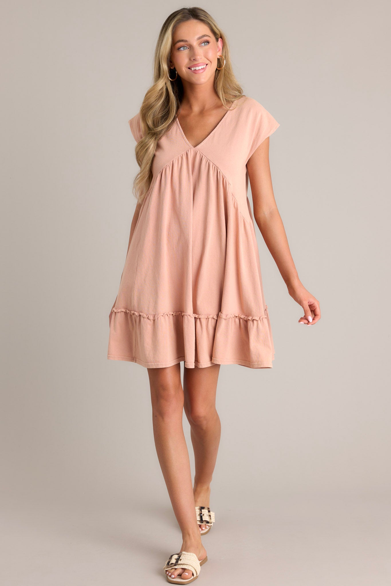 Action shot of a peach mini dress with a v-neckline, ruching below the bust line, and short cap sleeves, highlighting the flow and movement of the dress.