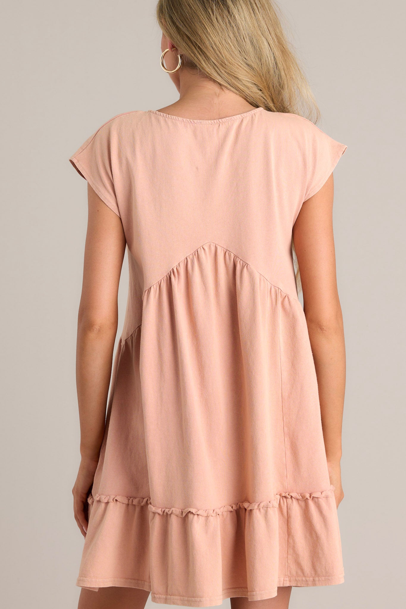 Back view of a peach mini dress showcasing the short cap sleeves and flowing silhouette.