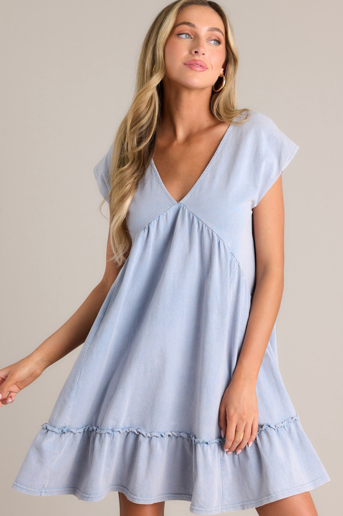 Action shot of a blue mini dress displaying the flow and movement of the fabric, highlighting the v-neckline, ruching below the bust line, and short cap sleeves.
