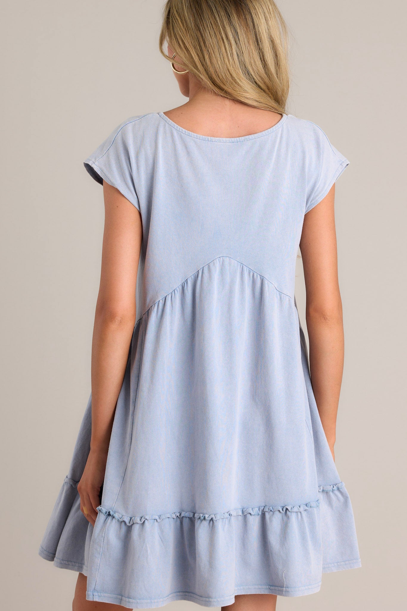 Back view of a blue mini dress highlighting the ruching below the bust line and the short cap sleeves.