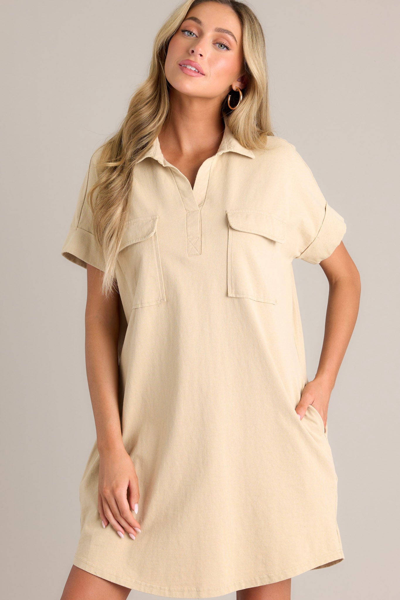 Angled front view of this tan mini dress that features a collared neckline, functional breast & hip pockets, and cuffed short sleeves.