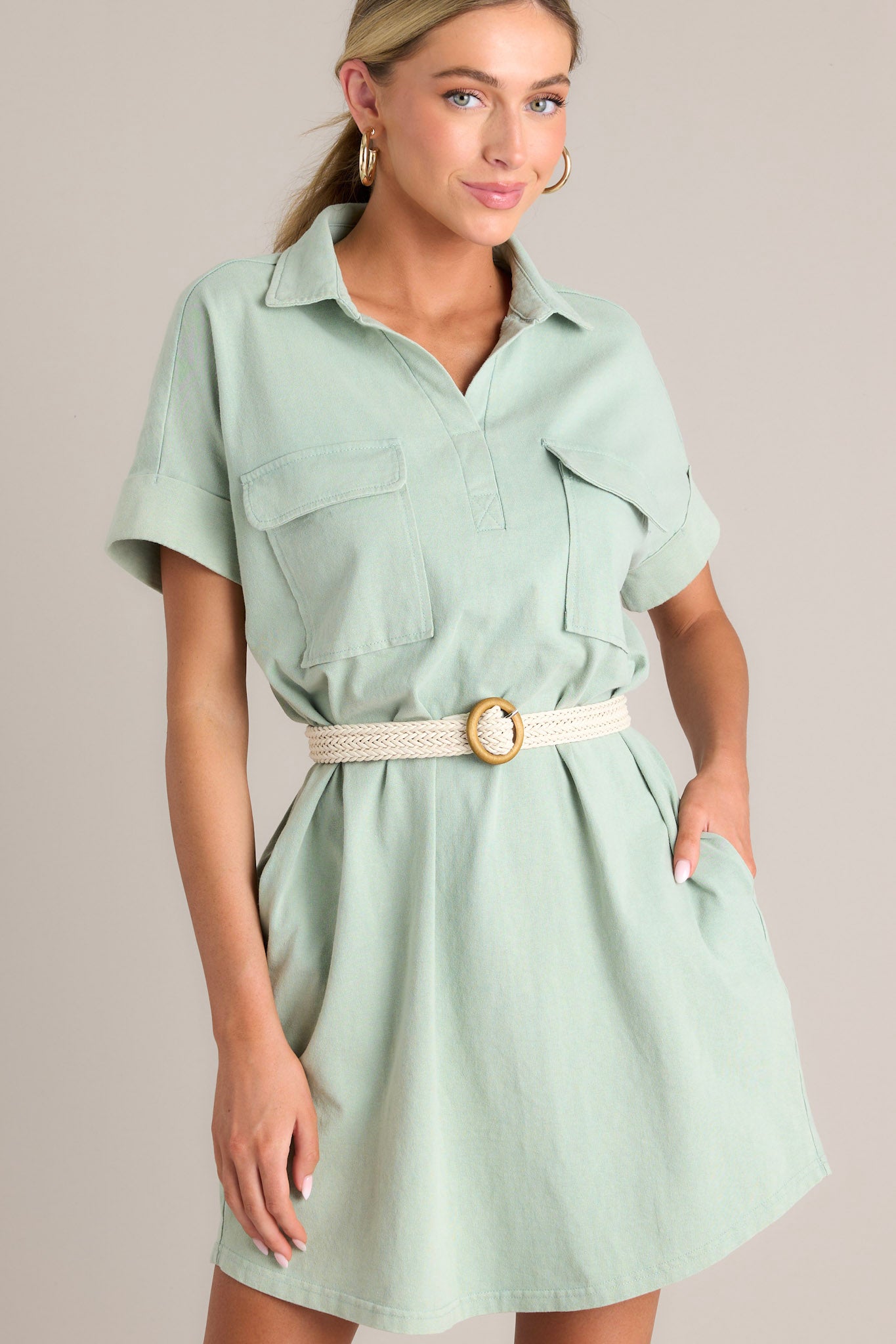 Front view of a sage green mini dress featuring a collared neckline, functional breast and hip pockets, relaxed fit, and cuffed short sleeves.