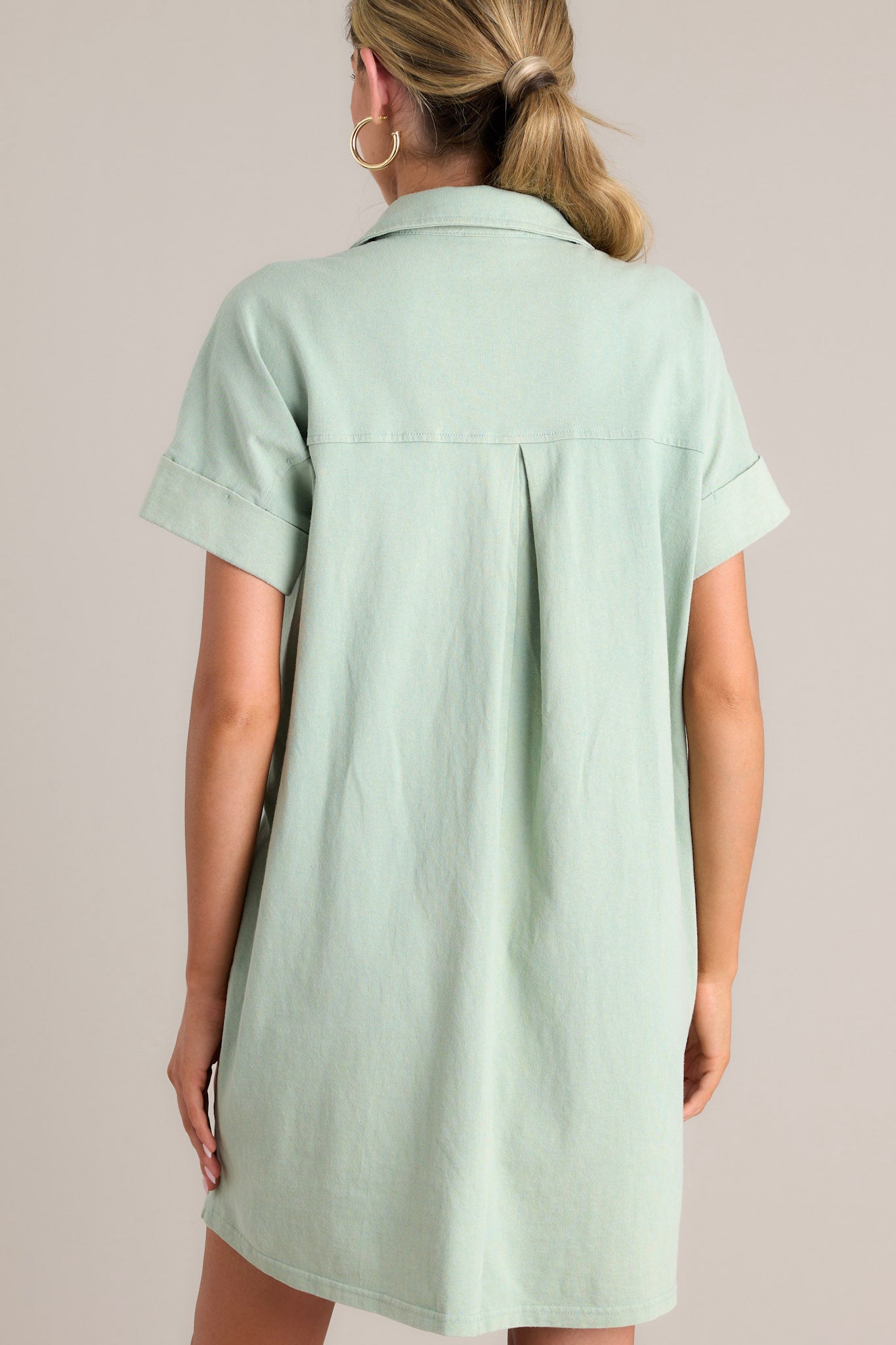 Back view of a sage green mini dress showcasing the collared neckline, relaxed fit, and cuffed short sleeves.