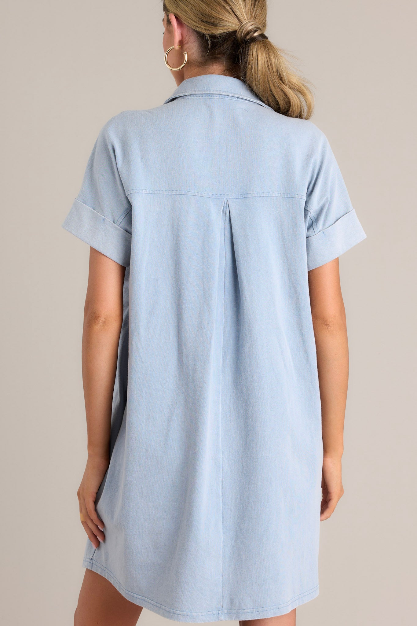 Back view of this light chambray mini dress that features a collared neckline, functional breast & hip pockets, a relaxed fit, and cuffed short sleeves.+