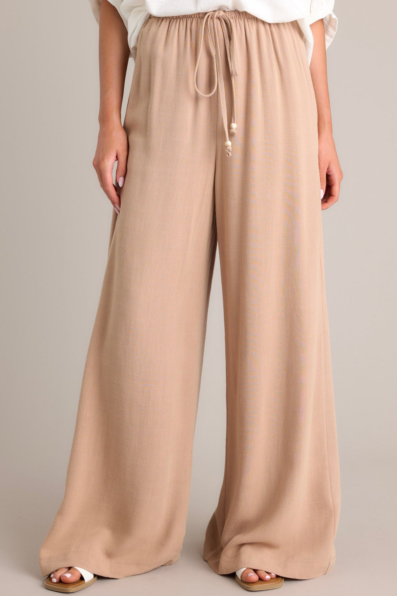 Tan high-waisted pants with thin elastic waistband, self-tie drawstring, functional hip pockets, and wide leg.