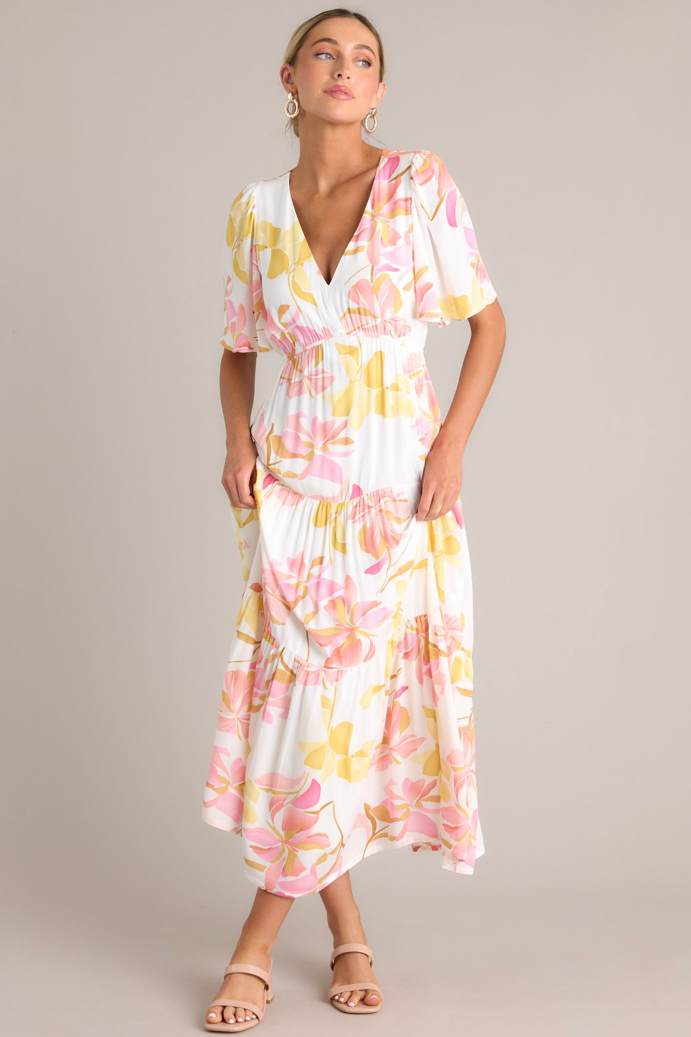 Angled full body view of this floral maxi dress that features a v-neckline, an elastic waistband, a tiered design, and short flutter sleeves.