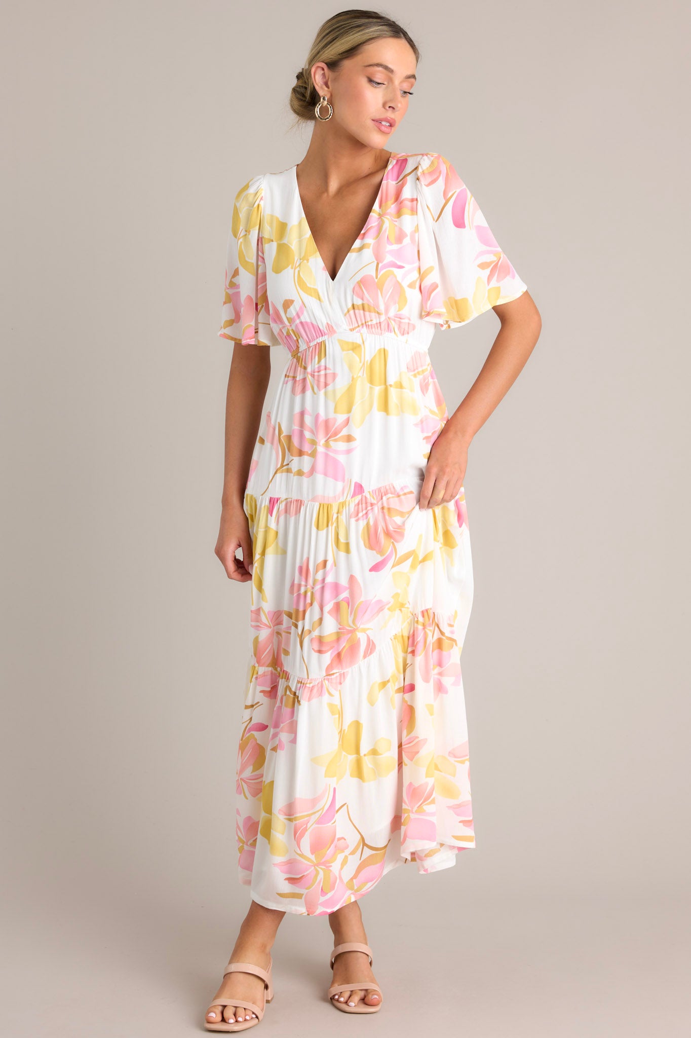 Angled front view of this floral maxi dress that features a v-neckline, an elastic waistband, a tiered design, and short flutter sleeves.