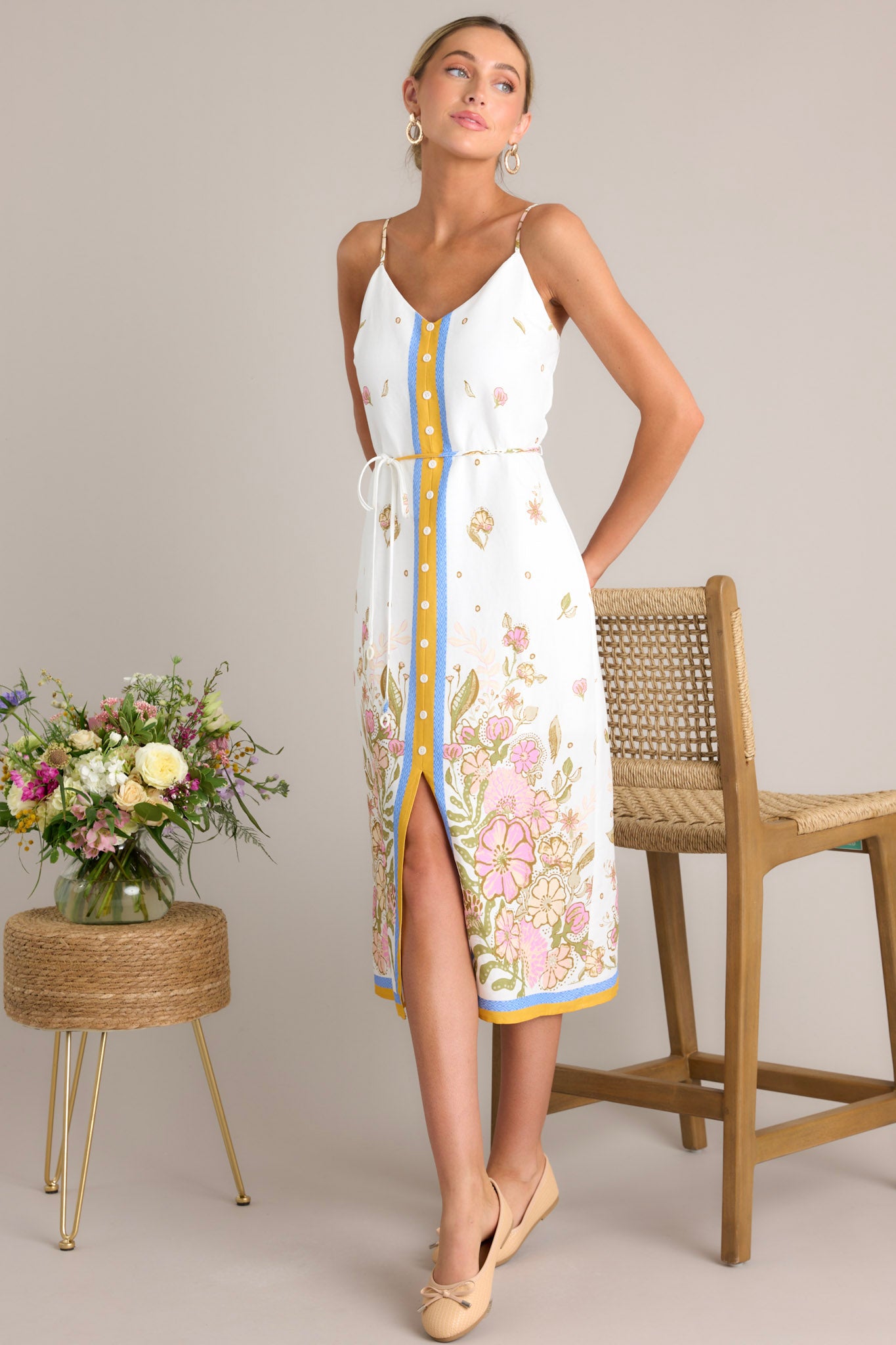 This ivory midi dress features a v-neckline, a discrete back zipper, thin adjustable straps, a faux button front, a self-tie waist belt, and a front slit.