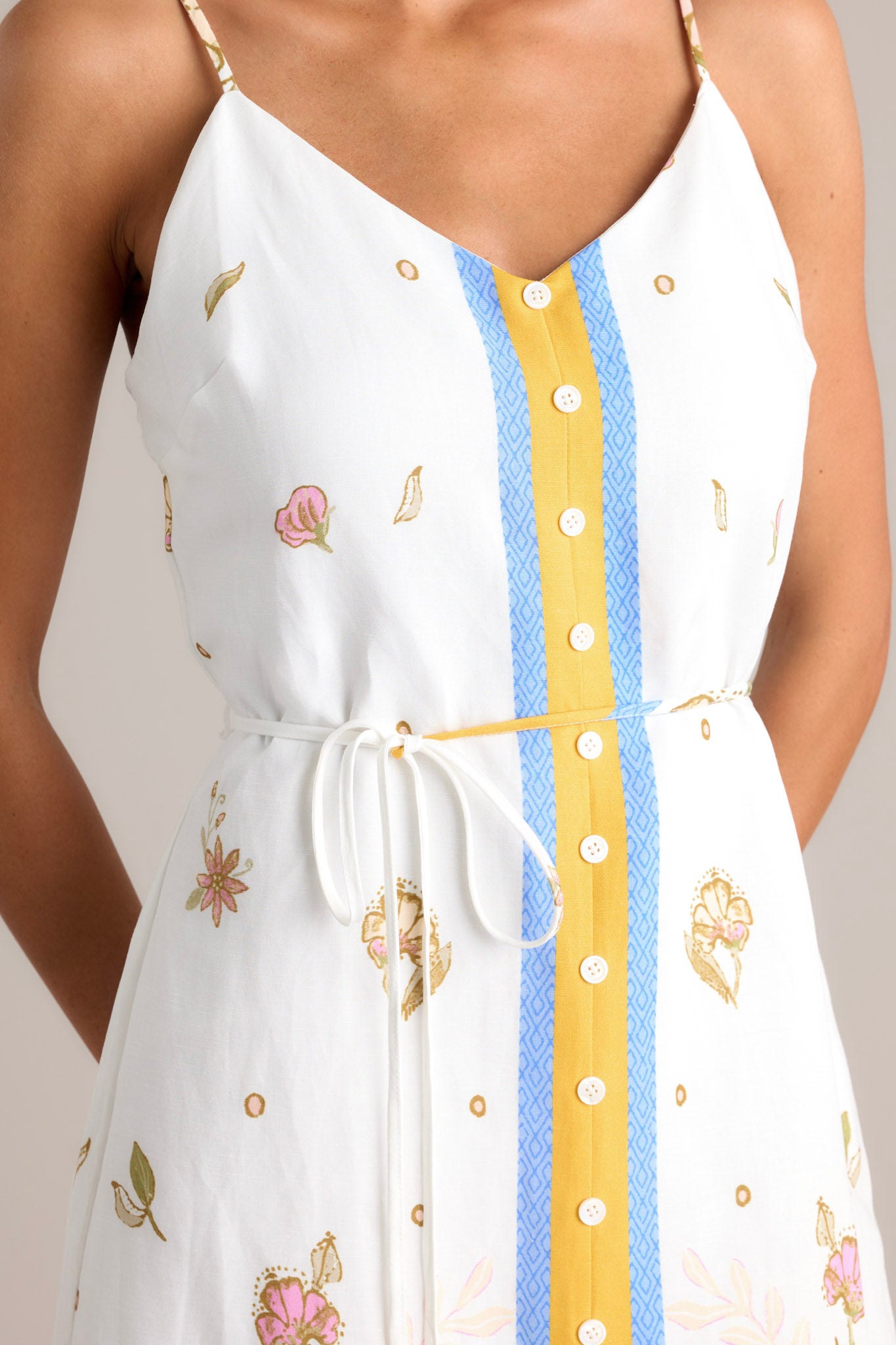 Close up view of this ivory midi dress features a v-neckline, a discrete back zipper, thin adjustable straps, a faux button front, a self-tie waist belt, and a front slit.