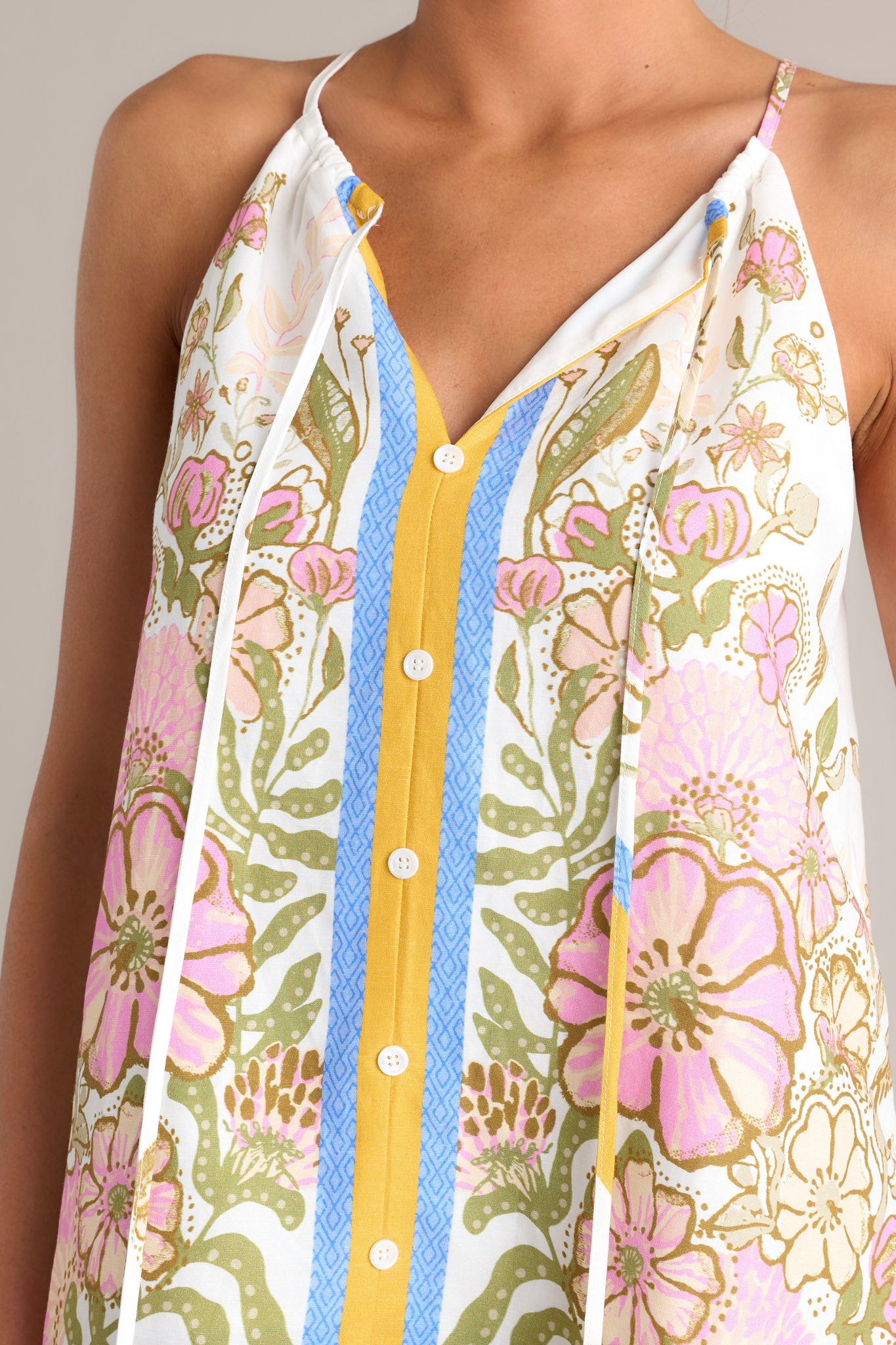 Close up view of this  ivory tank top with a v-neckline featuring a self-tie feature, thin straps, a faux button front, and a unique floral pattern.