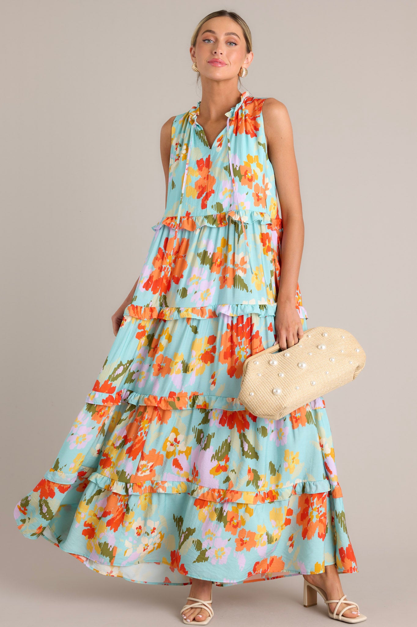 Full body view of this floral maxi dress that features a ruffled v-neckline with a self-tie feature, functional hip pockets, an abstract floral print, and a tiered design.