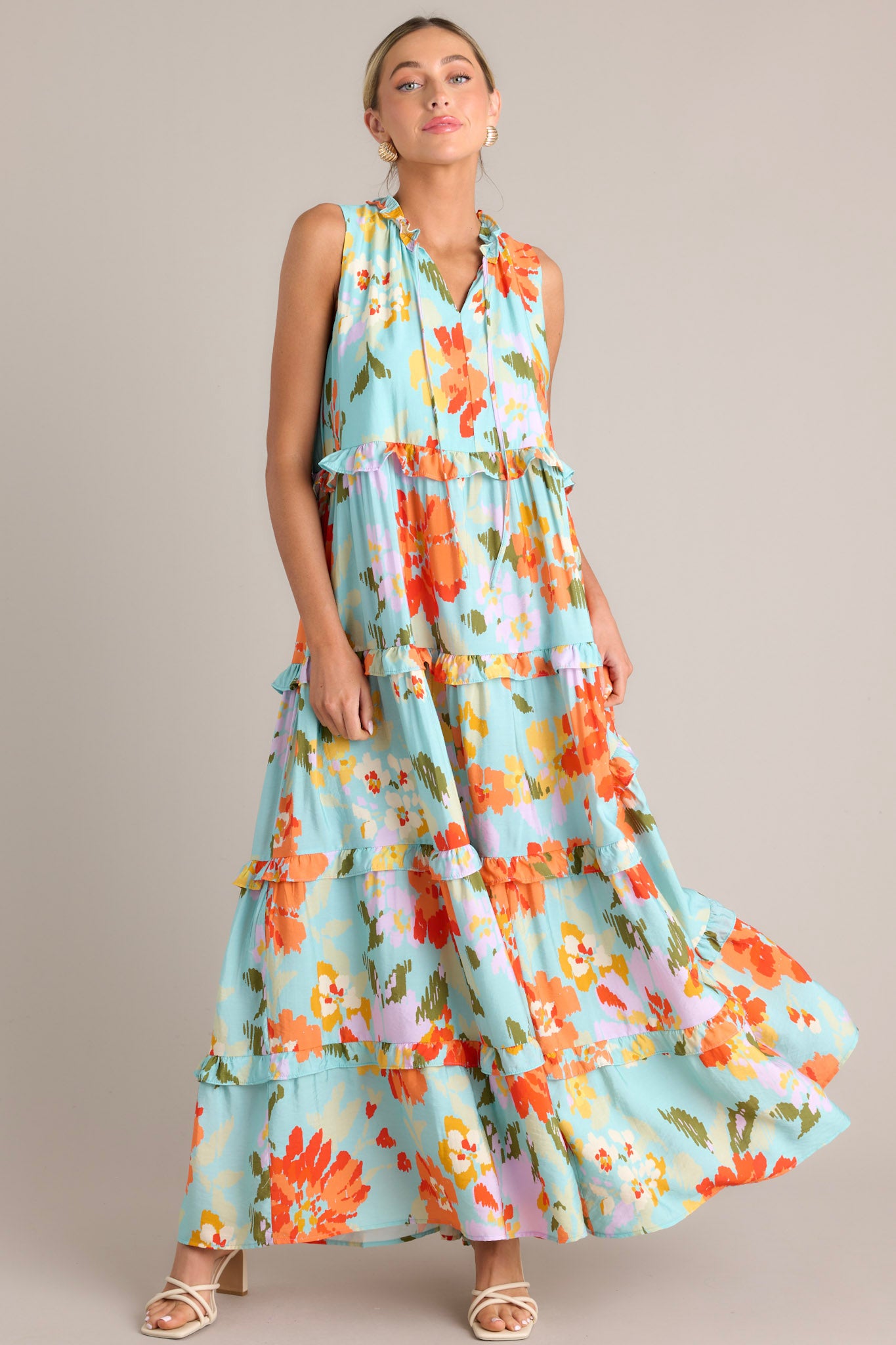 Angled full body view of this floral maxi dress that features a ruffled v-neckline with a self-tie feature, functional hip pockets, an abstract floral print, and a tiered design.