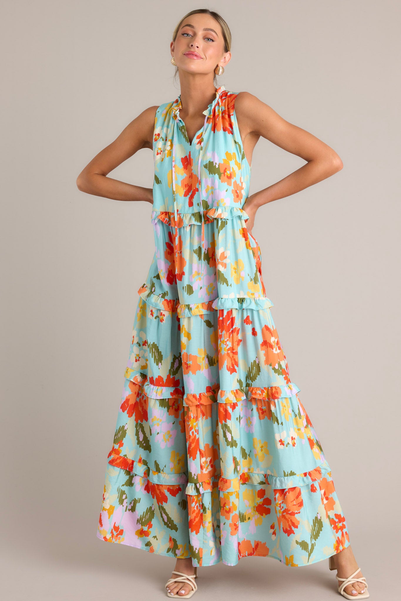 Front view of this floral maxi dress that features a ruffled v-neckline with a self-tie feature, functional hip pockets, an abstract floral print, and a tiered design.