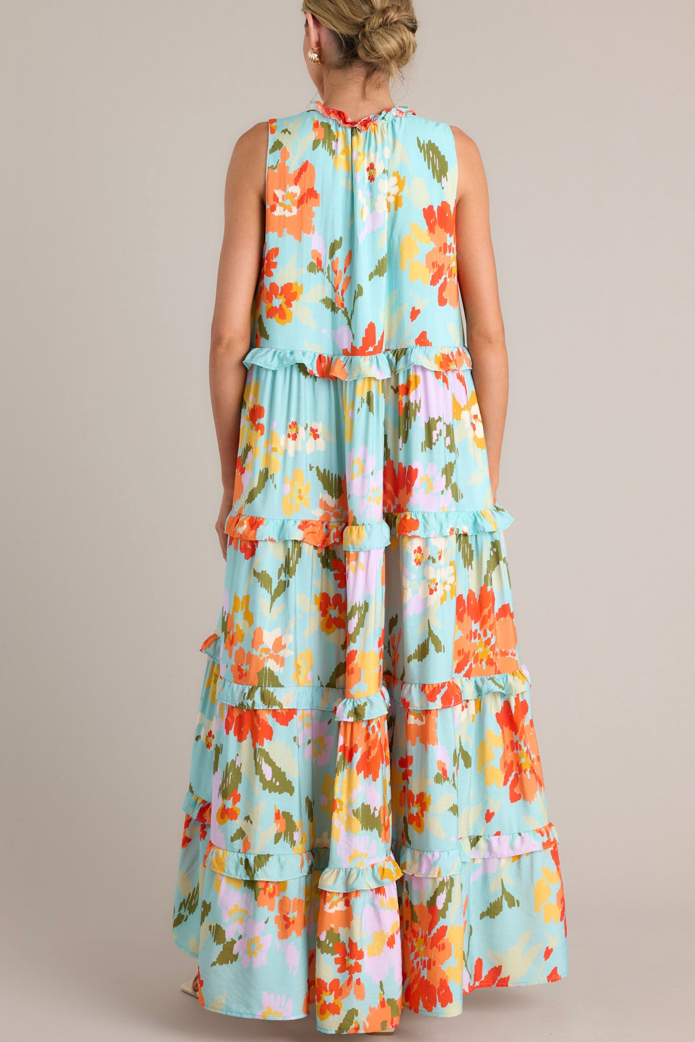 Back view of this floral maxi dress that features a ruffled v-neckline with a self-tie feature, functional hip pockets, an abstract floral print, and a tiered design.