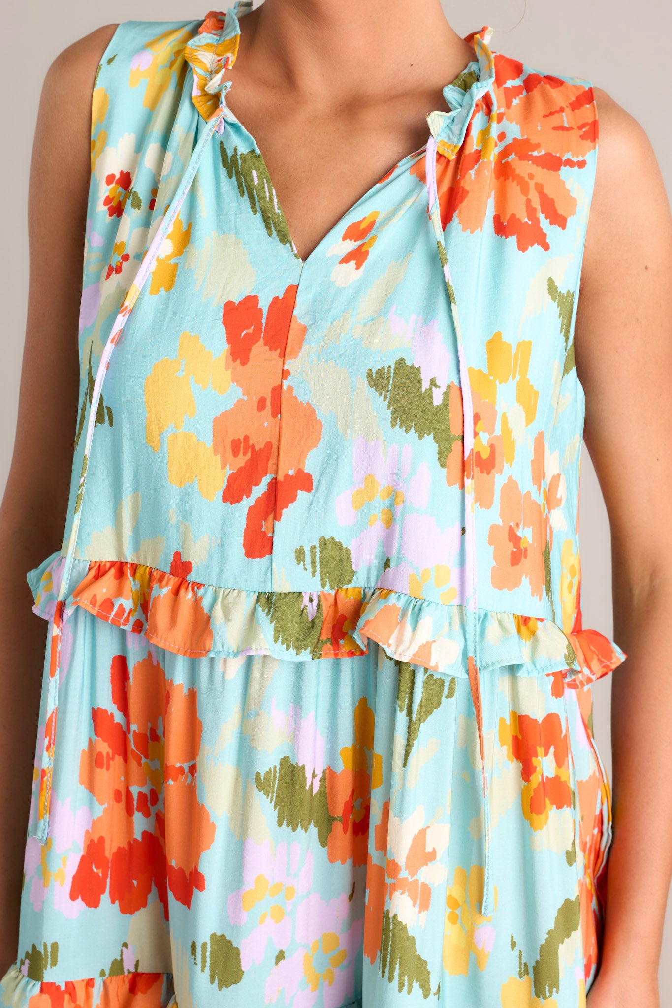 Close up view of this floral maxi dress that features a ruffled v-neckline with a self-tie feature, functional hip pockets, an abstract floral print, and a tiered design.