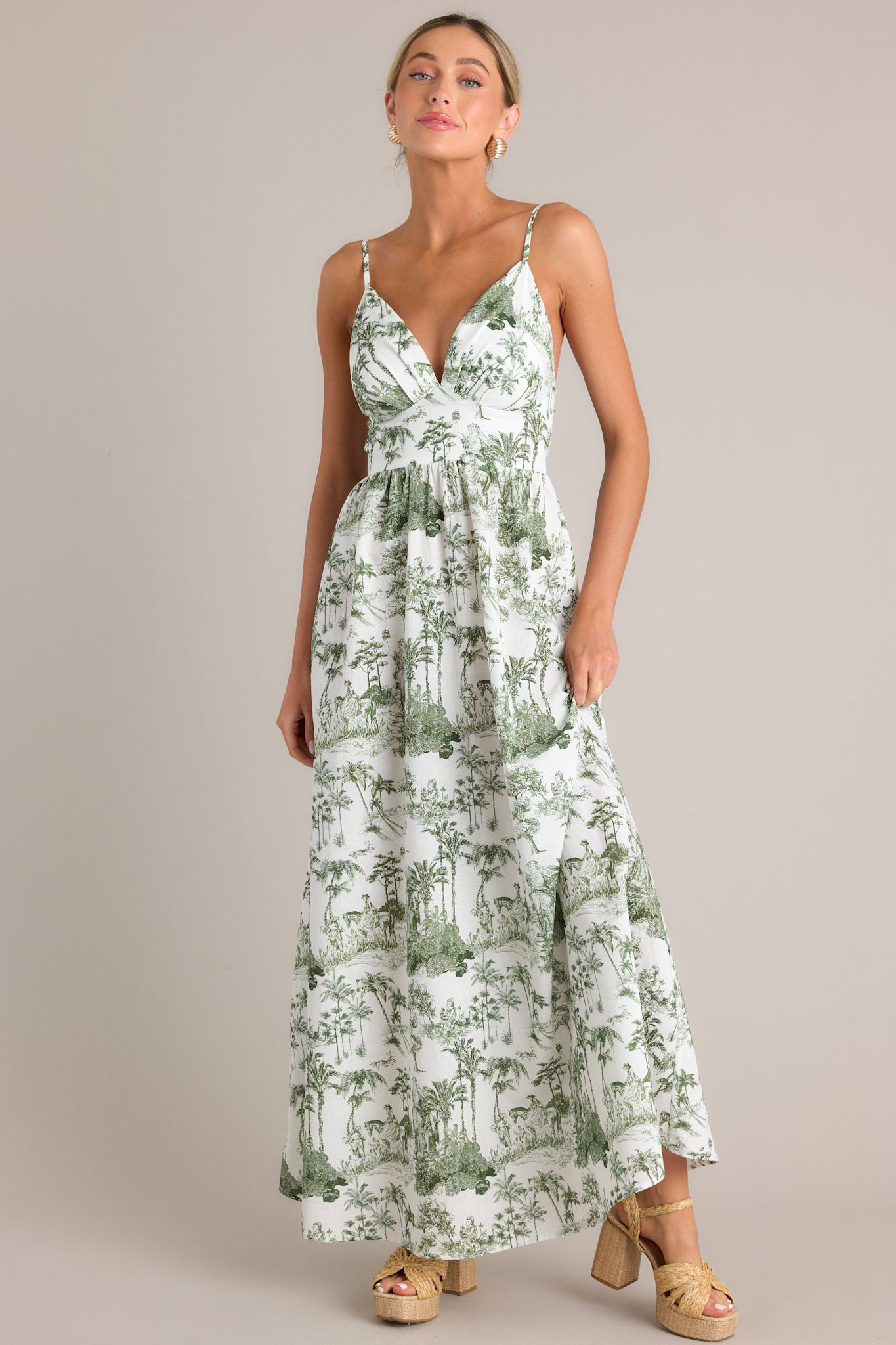 Full body view of this green toile maxi dress that features a v-neckline, thin adjustable straps, a slightly pleated bust, a smocked back insert, a thick waistband, and a flowing silhouette.