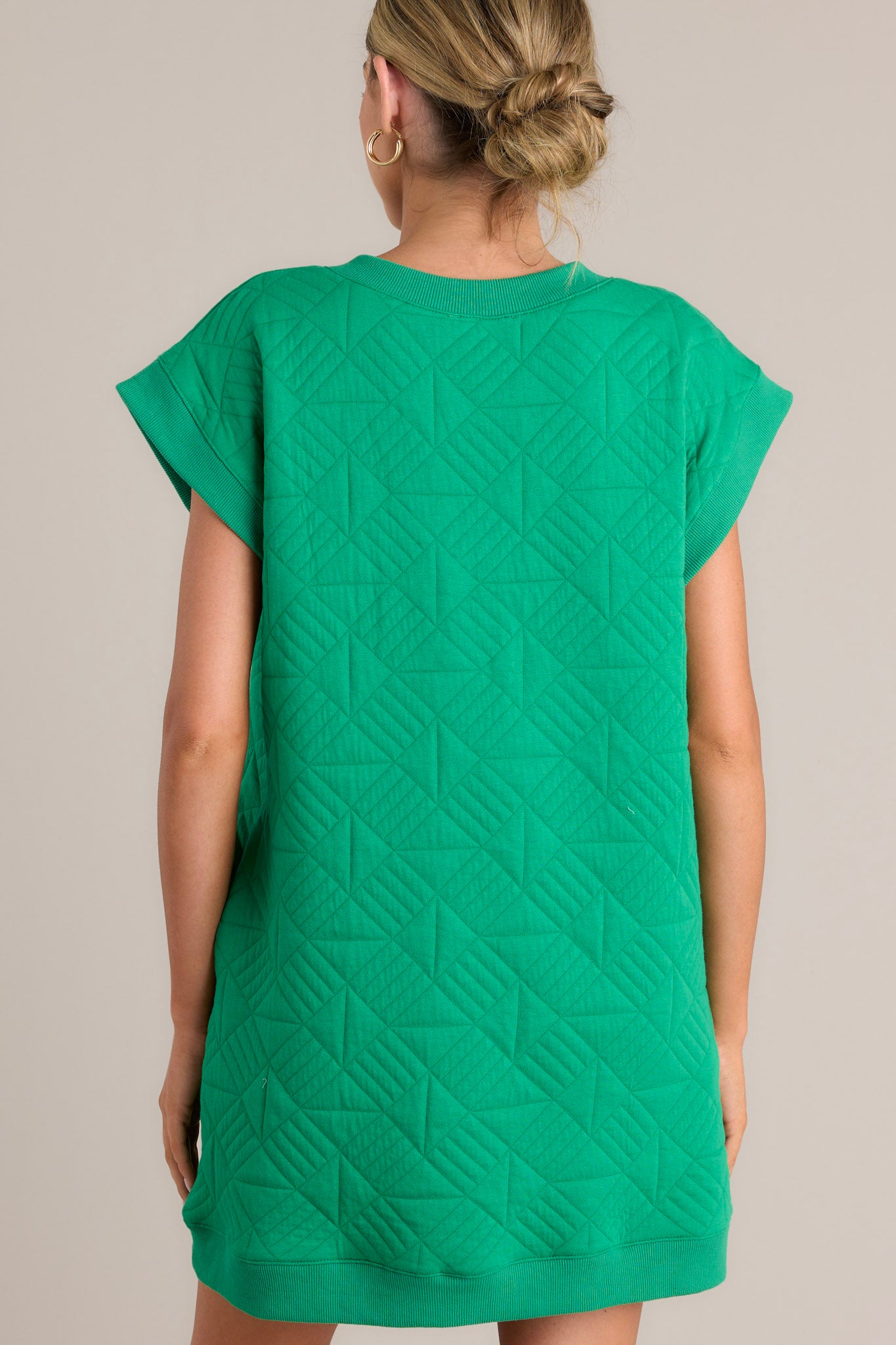 Back view of this green mini dress that features a v-neckline, an all over quilted design, functional hip pockets, and flattering cap sleeves.