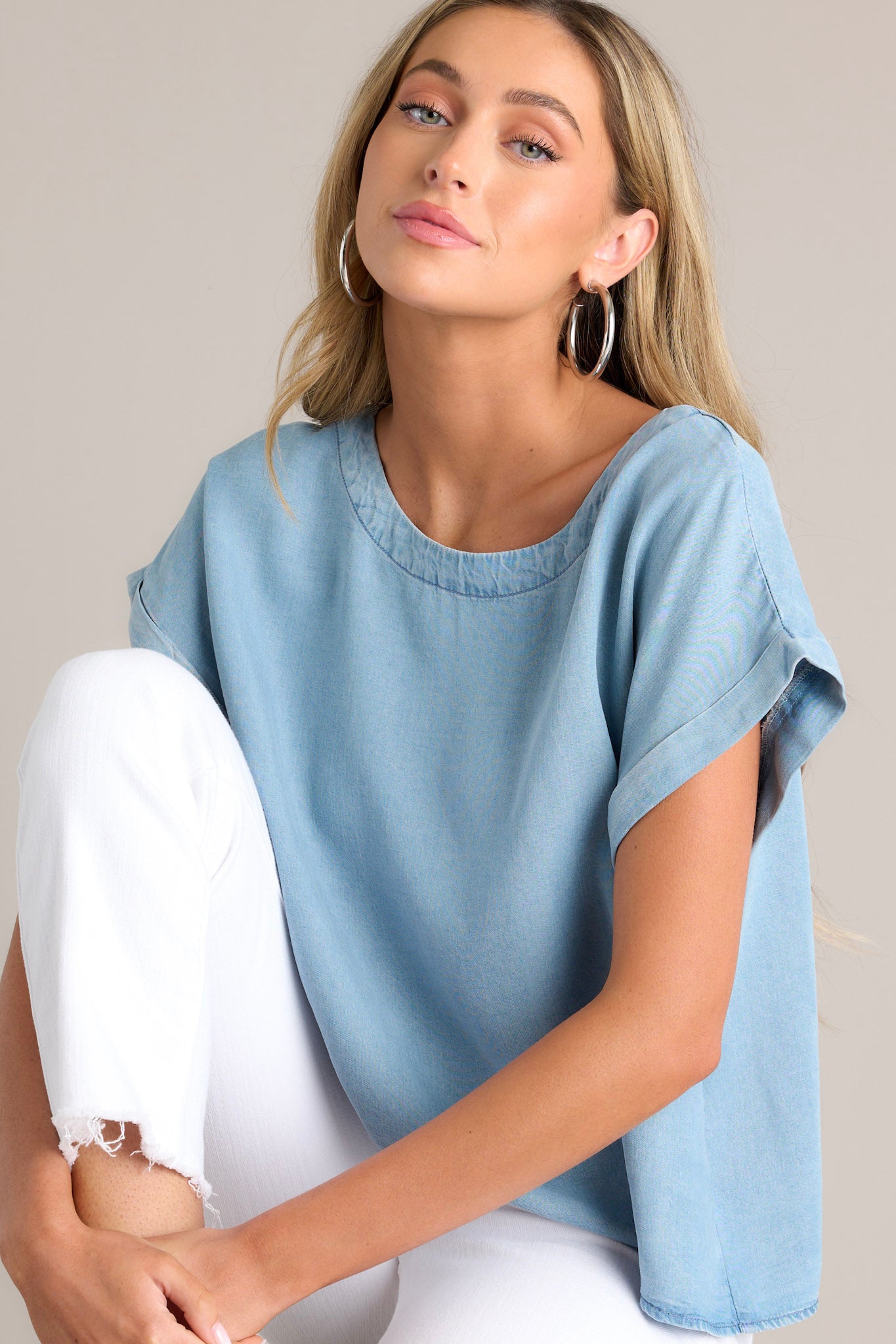 Seated close up view of this light chambray top that features a crew neckline, a relaxed fit, and a wide cuffed short sleeves.