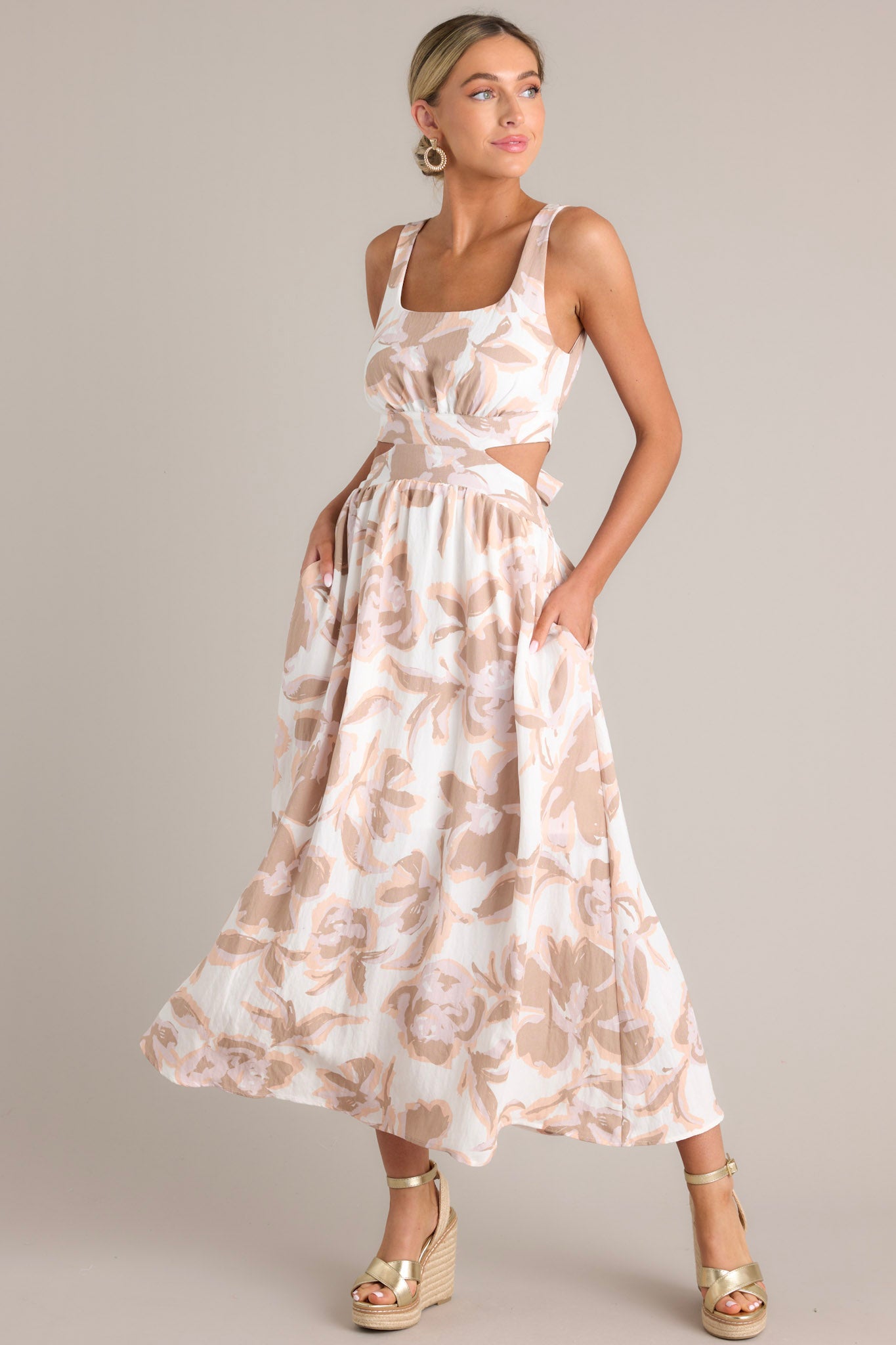 Action shot of a white maxi dress with a square neckline, thick straps, self-tie back feature, waist cutouts, functional hip pockets, and an all-over floral pattern, highlighting the flow and design.