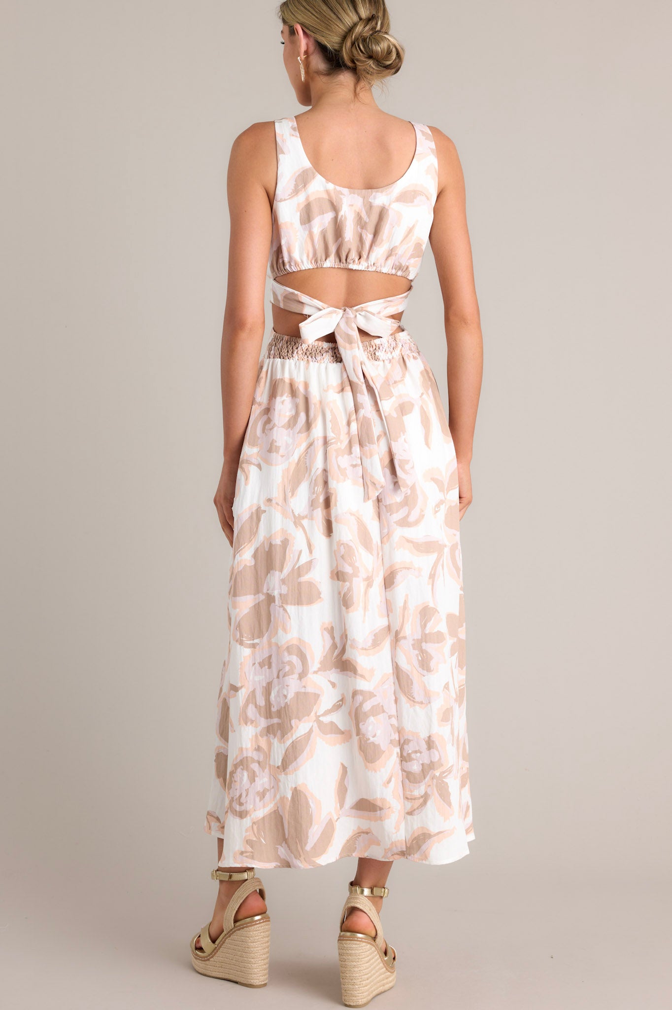 Back view of a white maxi dress showcasing the self-tie back feature, smocked back insert, thick straps, and all-over floral pattern.