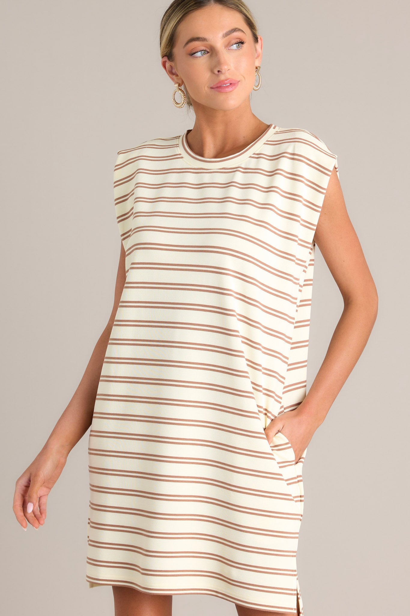 This stripe mini dress features a crew neckline, short cap sleeves, a double stripe pattern, functional hip pockets, and a split hemline.