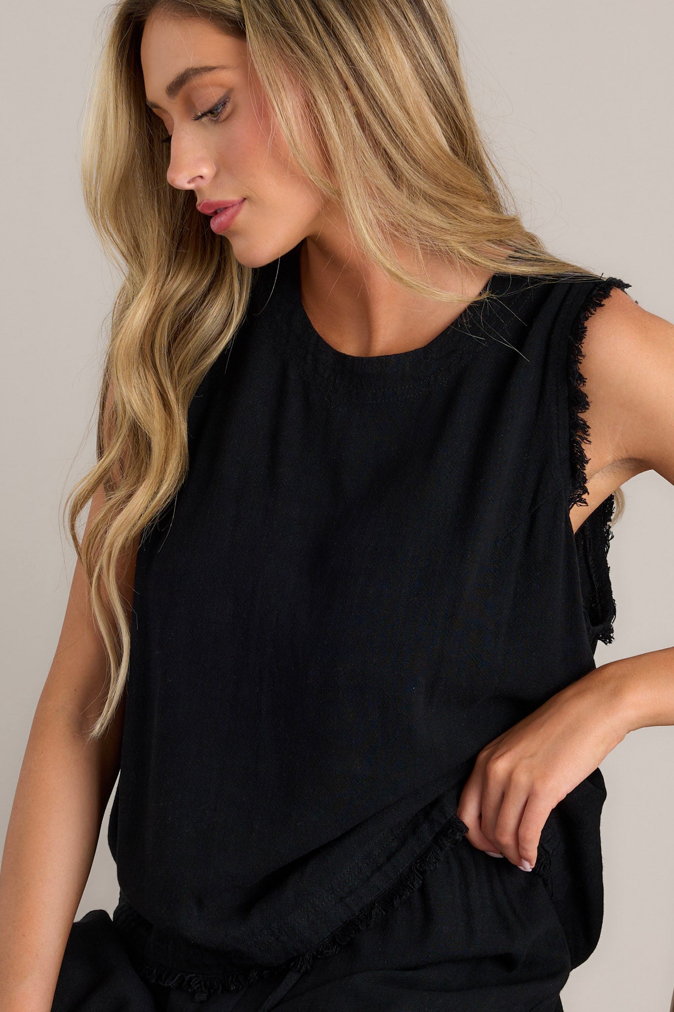 This black tank features a crew neckline, functional buttons down the back, frayed shoulders, and a frayed hemline.