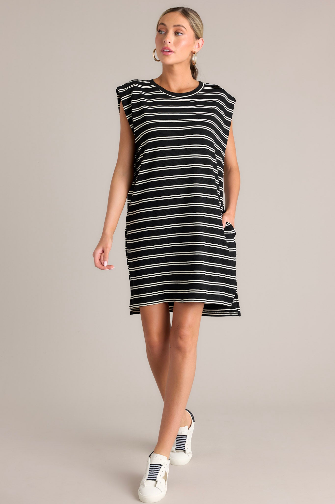 Full body angled view of this black stripe mini dress that features a crew neckline, short cap sleeves, a double stripe pattern, functional hip pockets, and a split hemline.