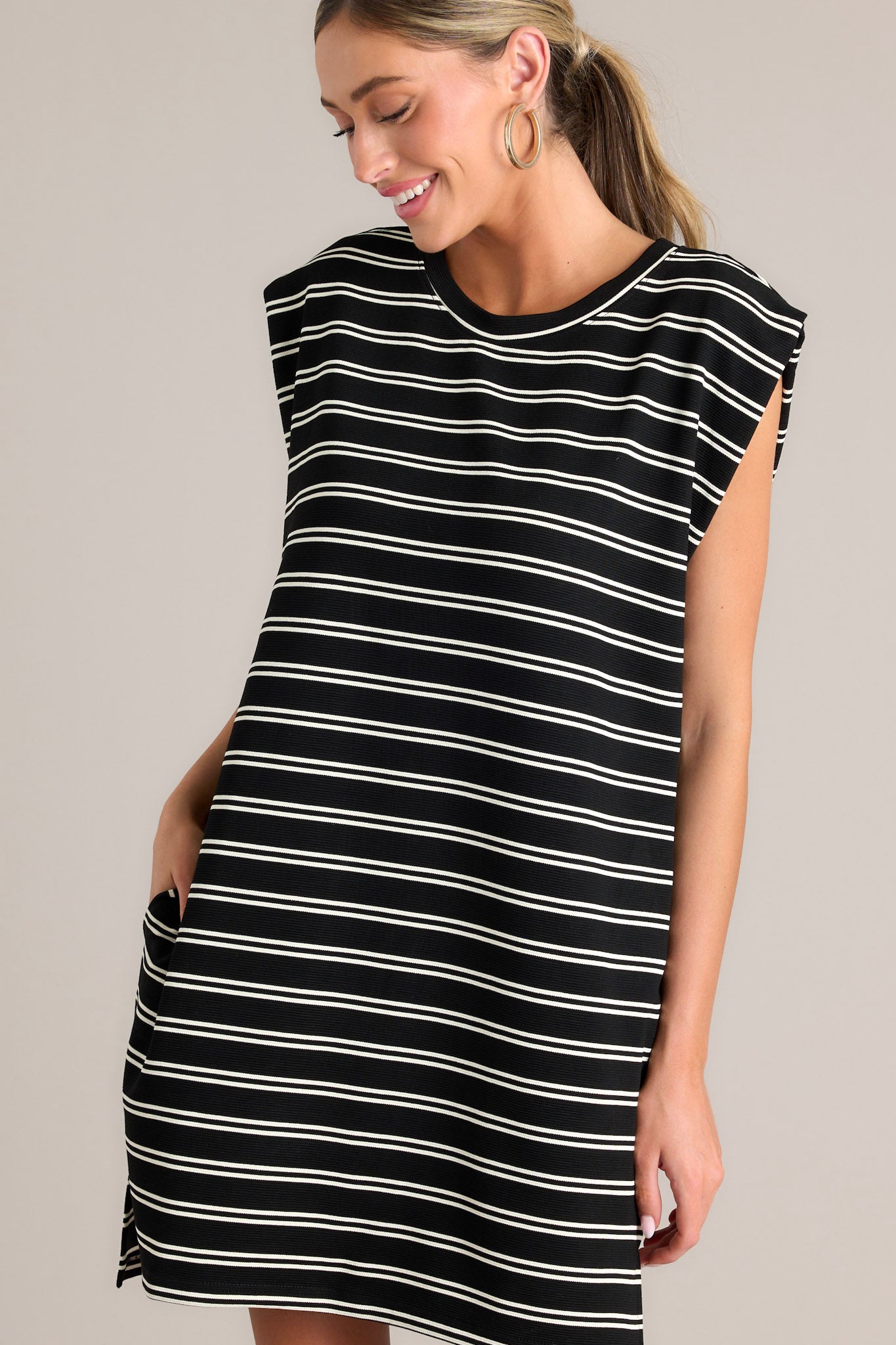 Angled close up view of this black stripe mini dress that features a crew neckline, short cap sleeves, a double stripe pattern, functional hip pockets, and a split hemline.