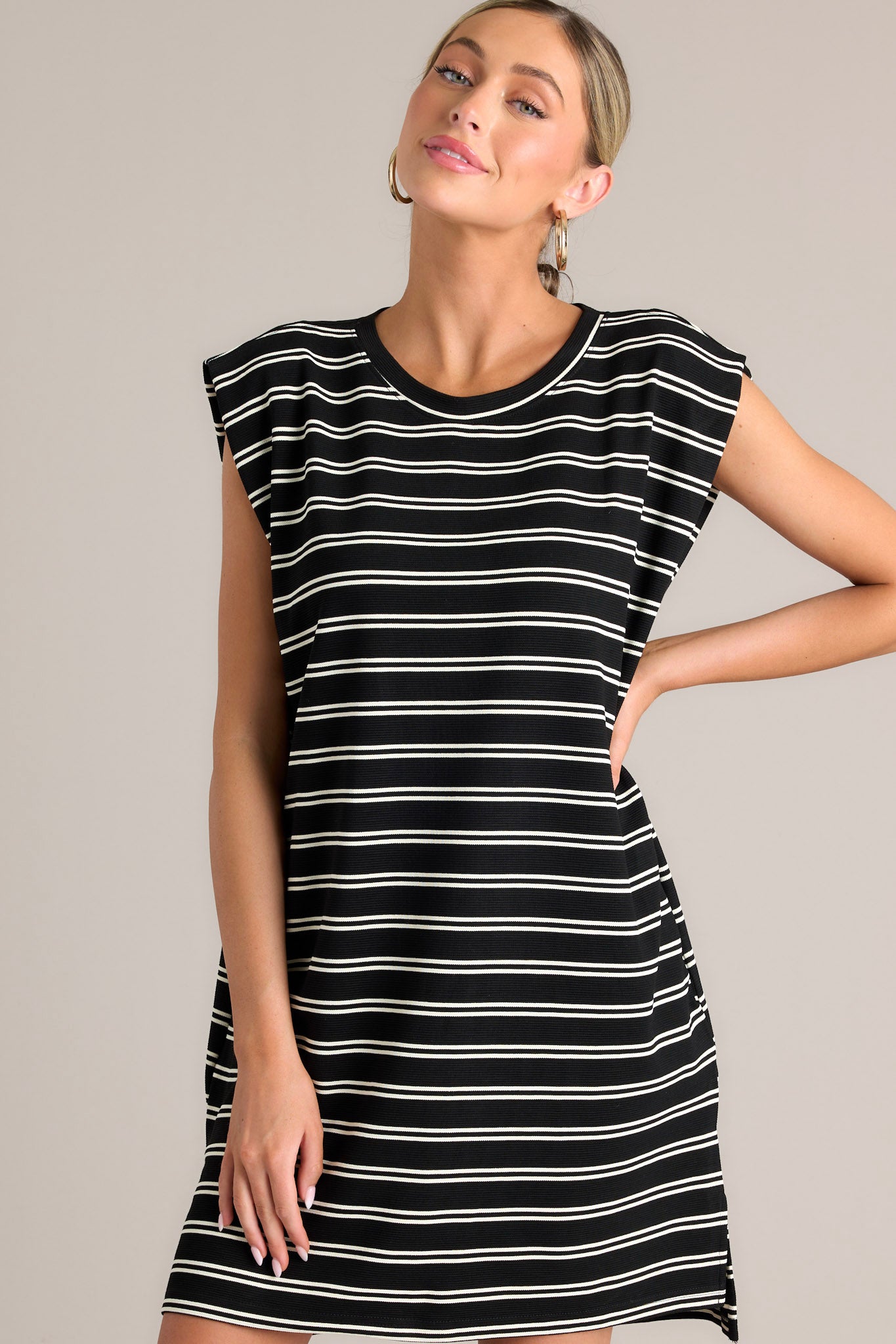 This black stripe mini dress features a crew neckline, short cap sleeves, a double stripe pattern, functional hip pockets, and a split hemline.