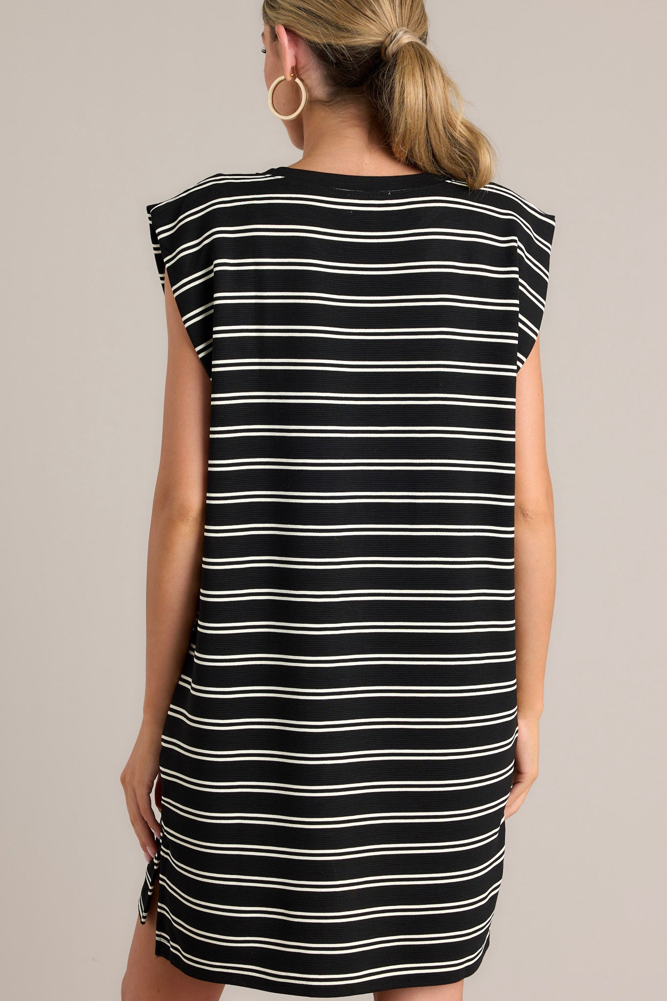 Back view of this black stripe mini dress that features a crew neckline, short cap sleeves, a double stripe pattern, functional hip pockets, and a split hemline.