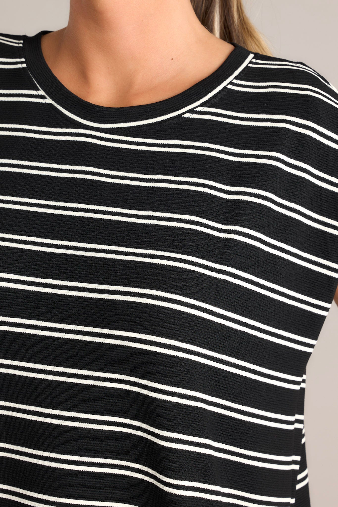 Close up view of this black stripe mini dress that features a crew neckline, short cap sleeves, a double stripe pattern, functional hip pockets, and a split hemline.