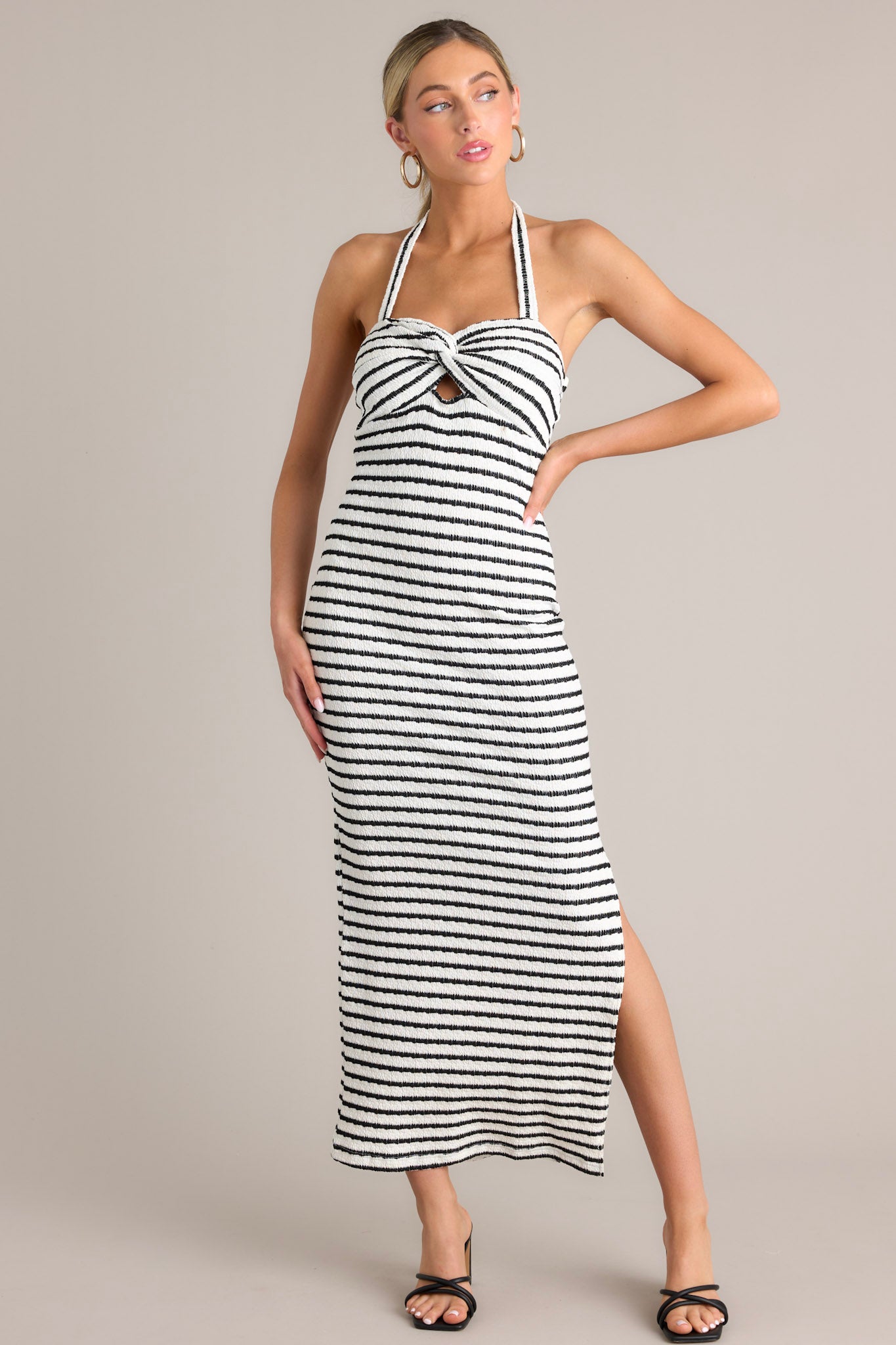 Front view of this stripe maxi dress that features a self-tie halter neckline, twist detailing in the bust, a chest cutout, an open back, a textured material, and a side slit.