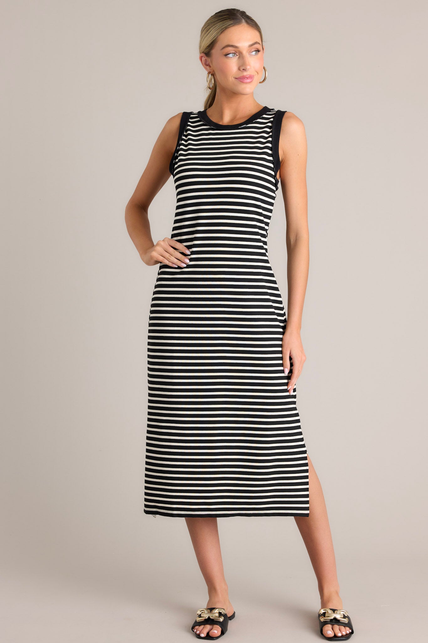 Angled full body view of this black stripe midi dress that features a crew neckline, a classic horizontal stripe design, and a split hemline.