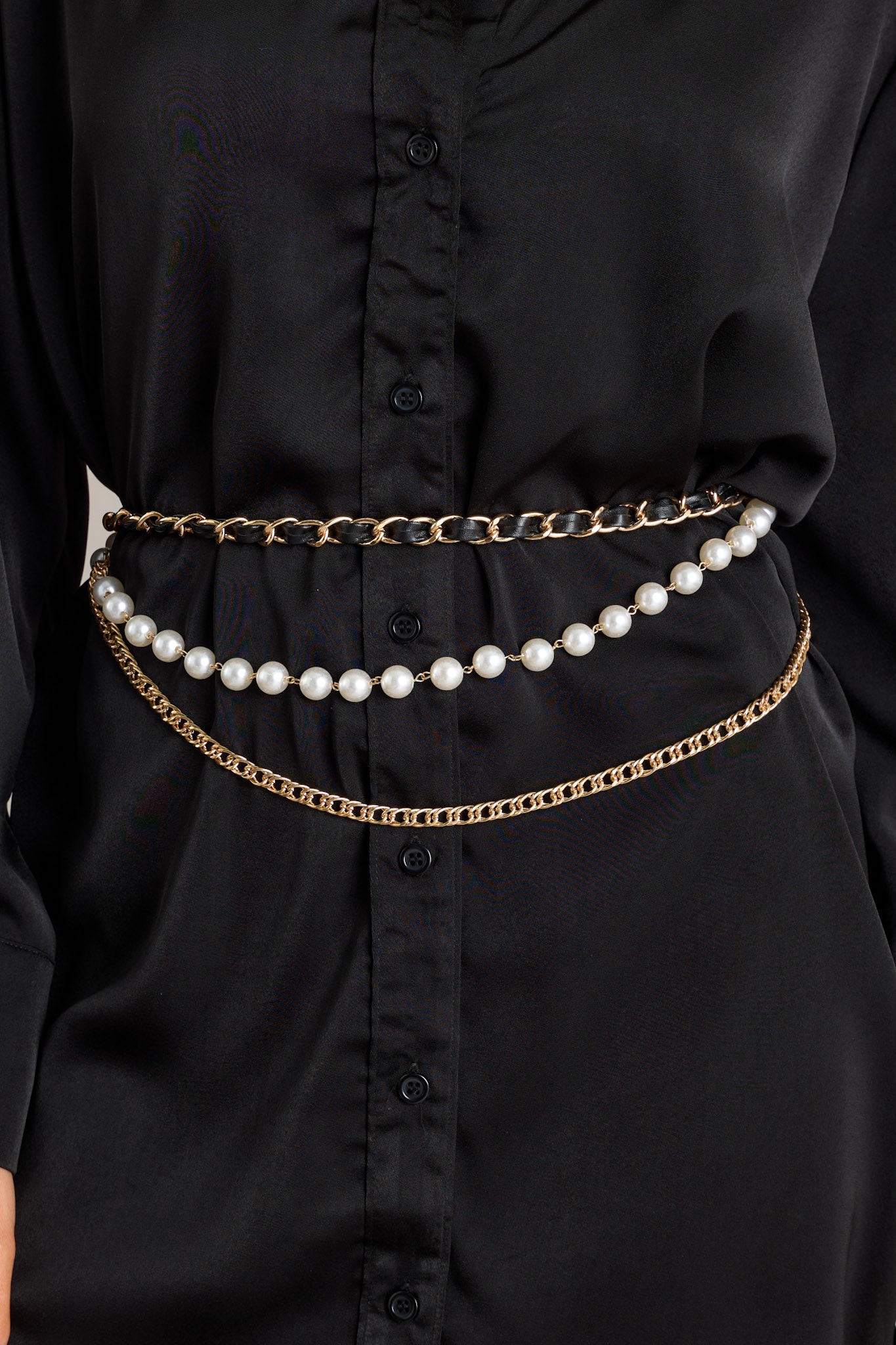 This chain belt features gold hardware, a black faux leather chain, a faux pearl chain, a curb chain belt, and a lobster claw closure.