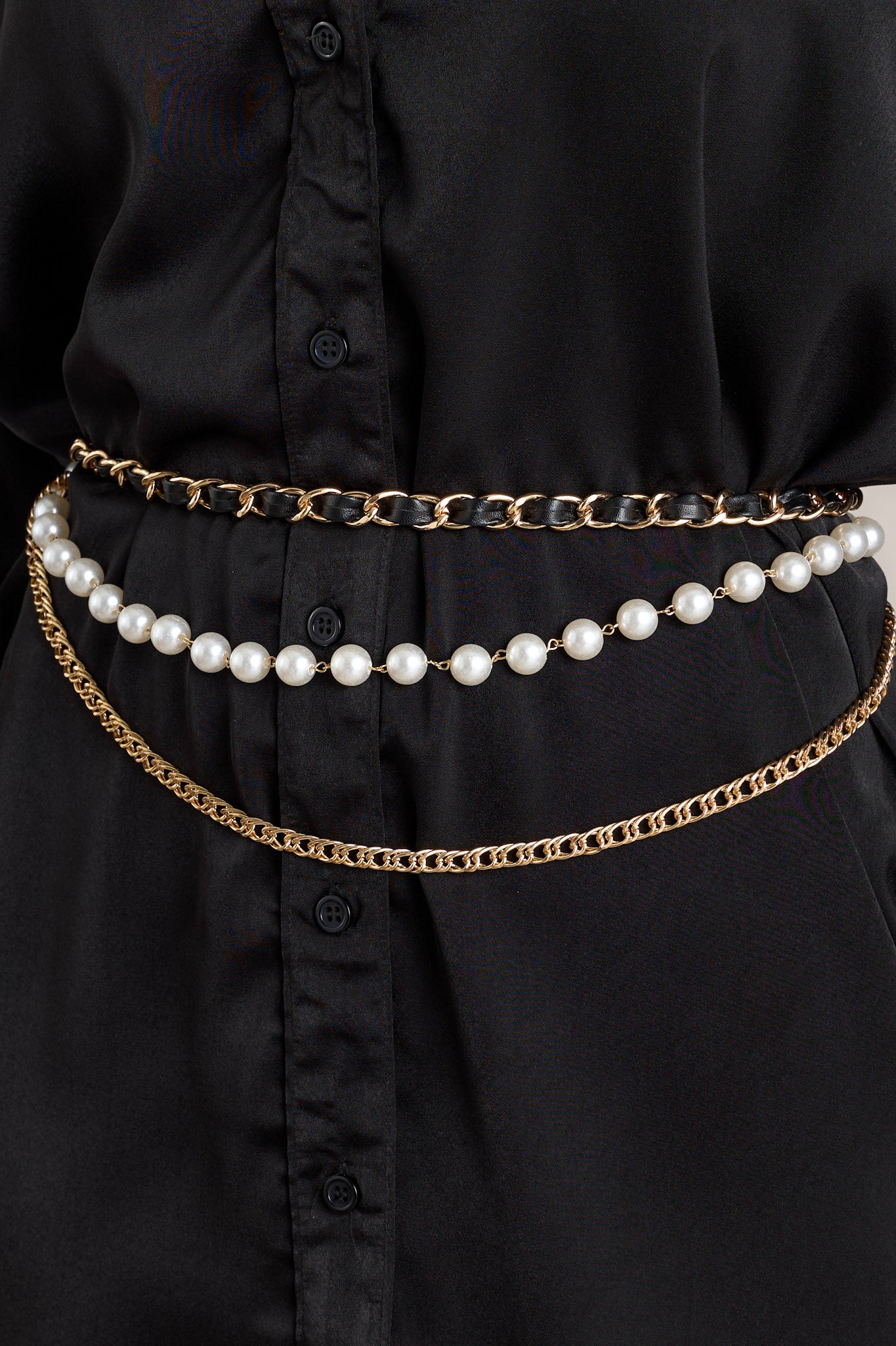 Close up view of this chain belt that features gold hardware, a black faux leather chain, a faux pearl chain, a curb chain belt, and a lobster claw closure.