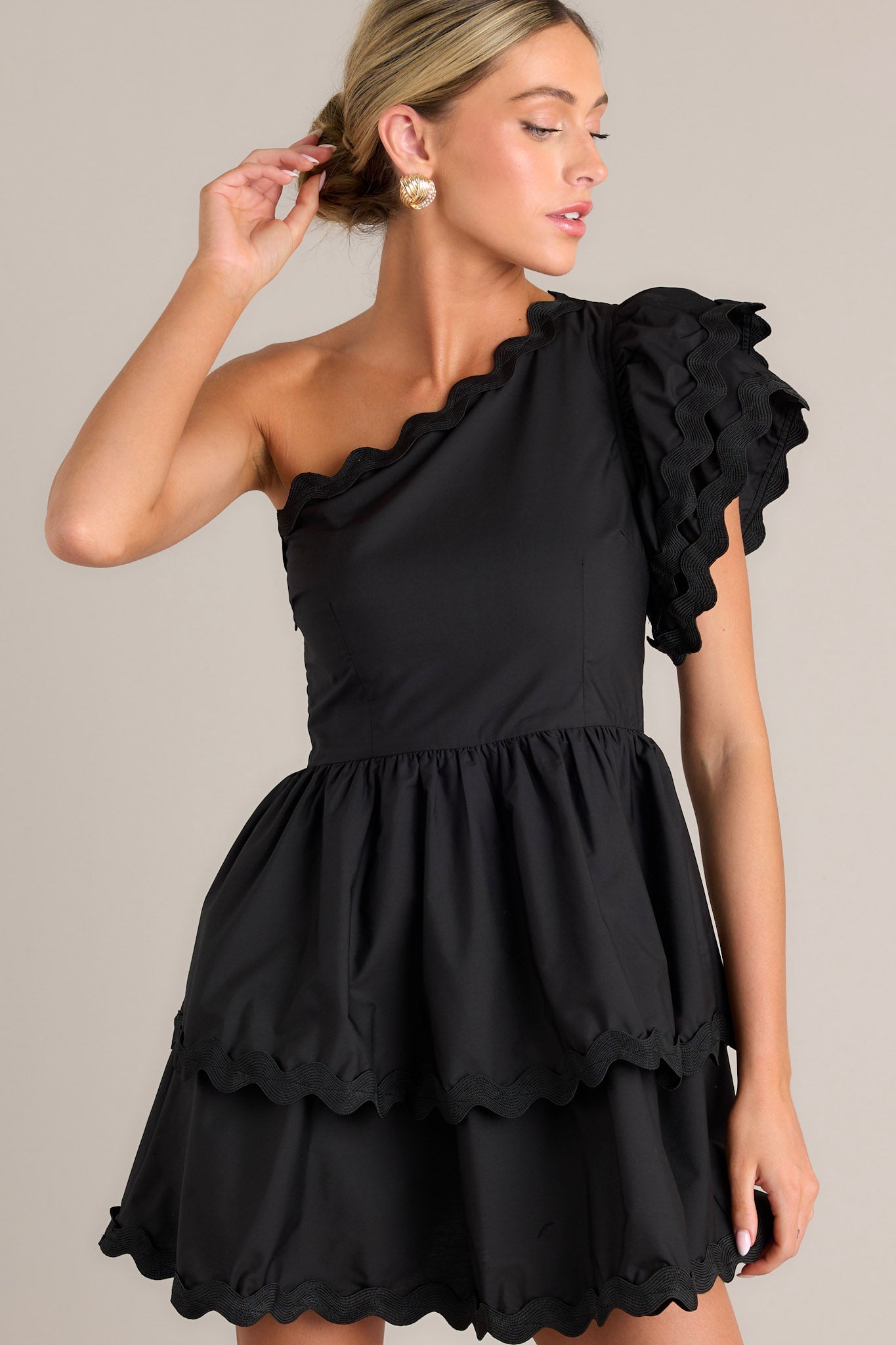 This black romper features rick rack scalloped hems, a one shoulder neckline, a flutter sleeve, a side zipper closure, and a tiered skirt with built in shorts.