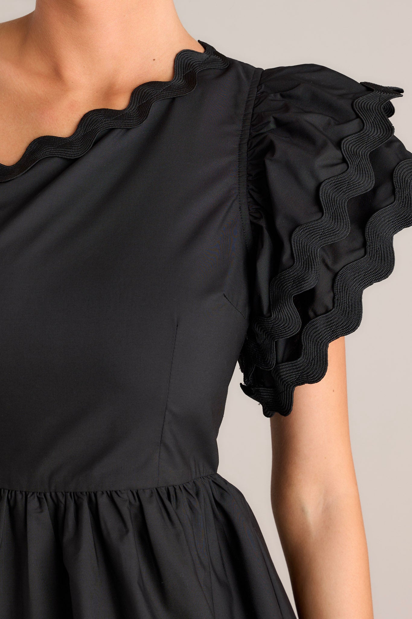 Close up view of the scallop detailing on the sleeve of this black one shoulder romper