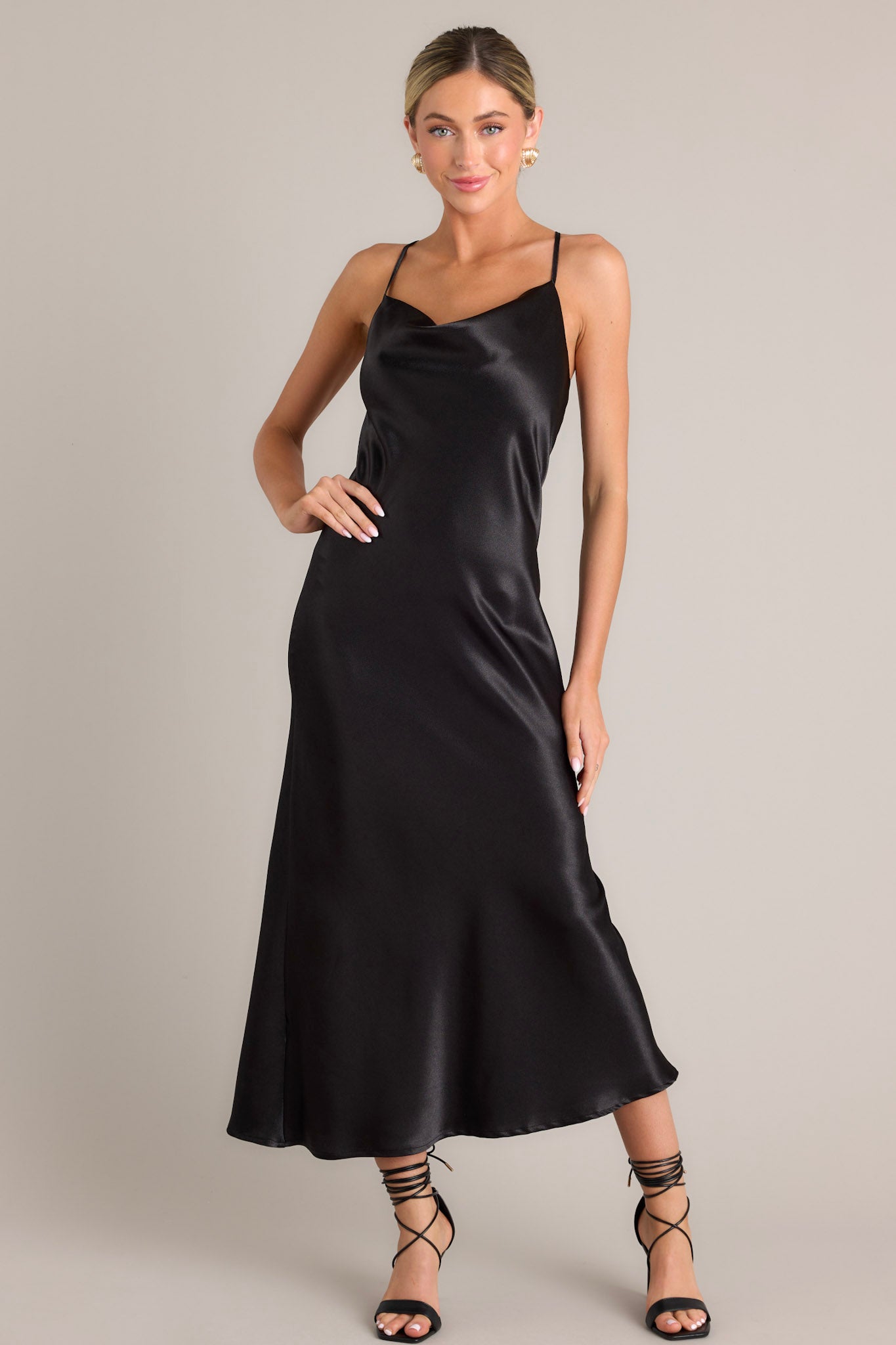 Front view of this elegant black dress that features a satin-like fabric, adjustable straps, and a cowl neckline.